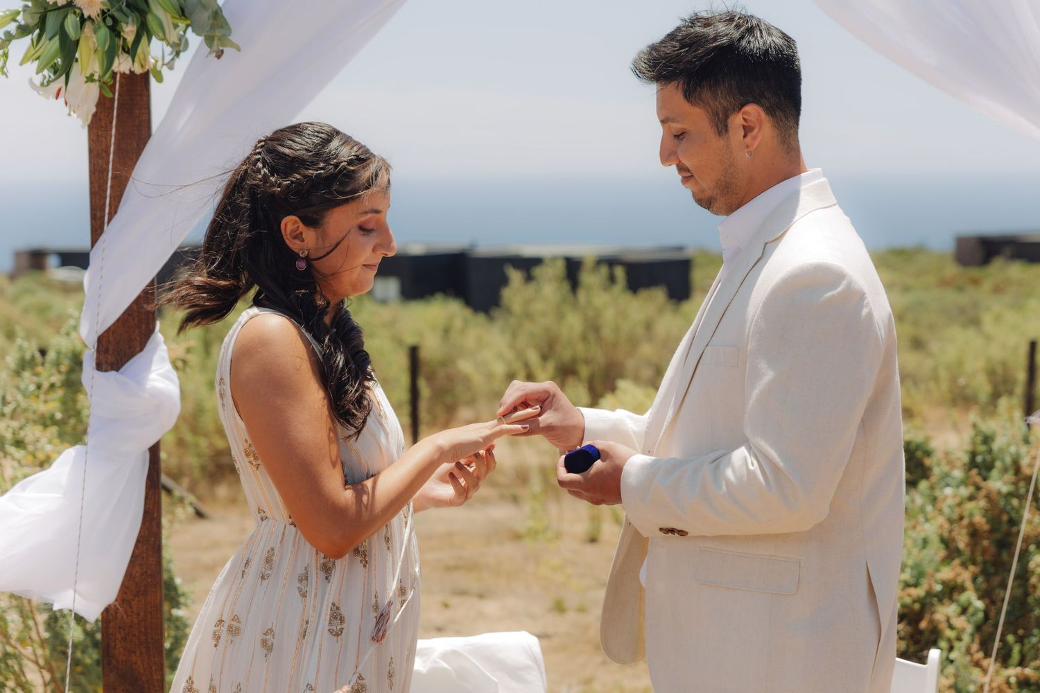 Groom sliding a wedding ring onto the brides finger during an intimate outdoor ceremony with natural landscape backdrop.