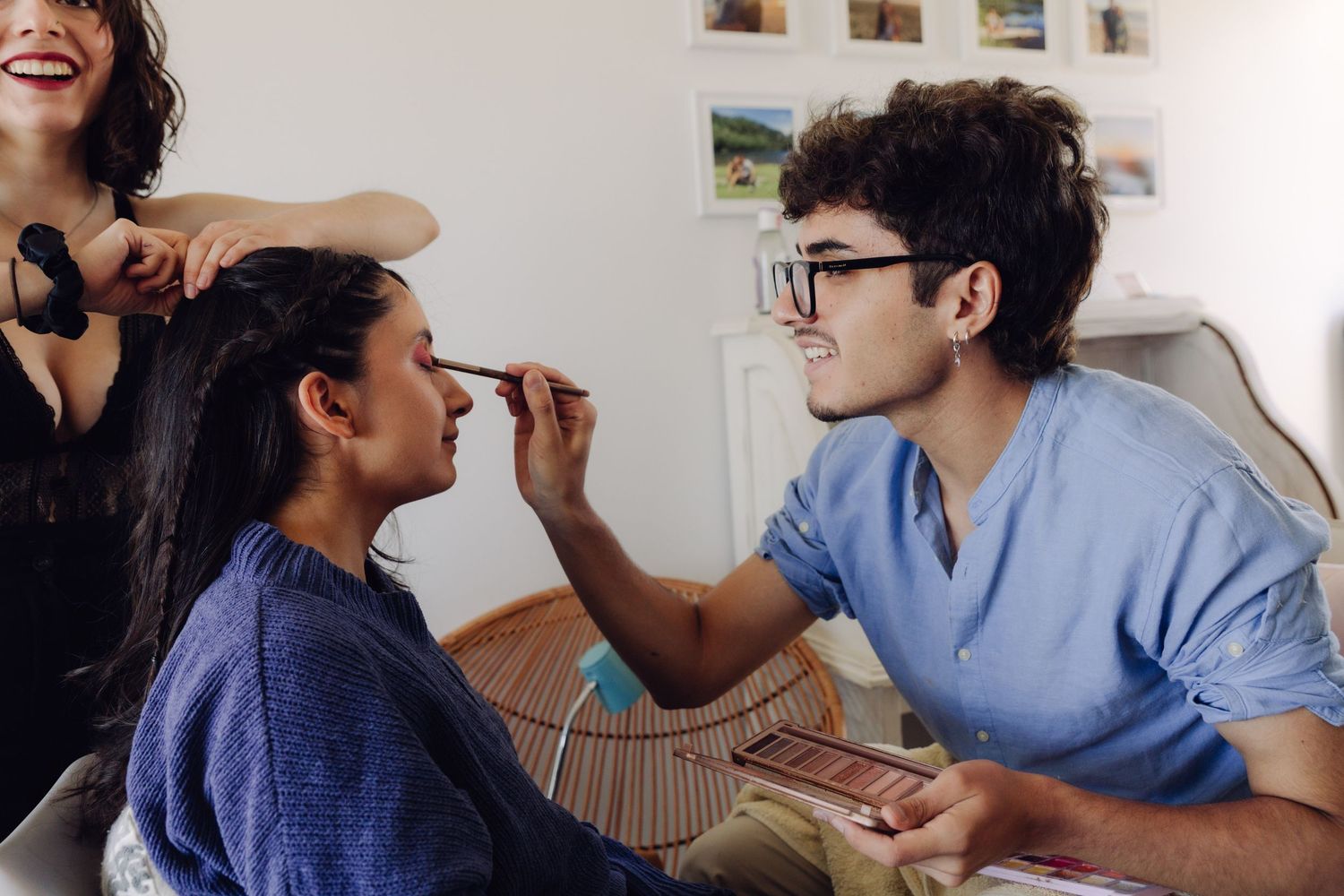 Makeup artist applying eyeshadow to smiling bride during wedding preparation indoors.
