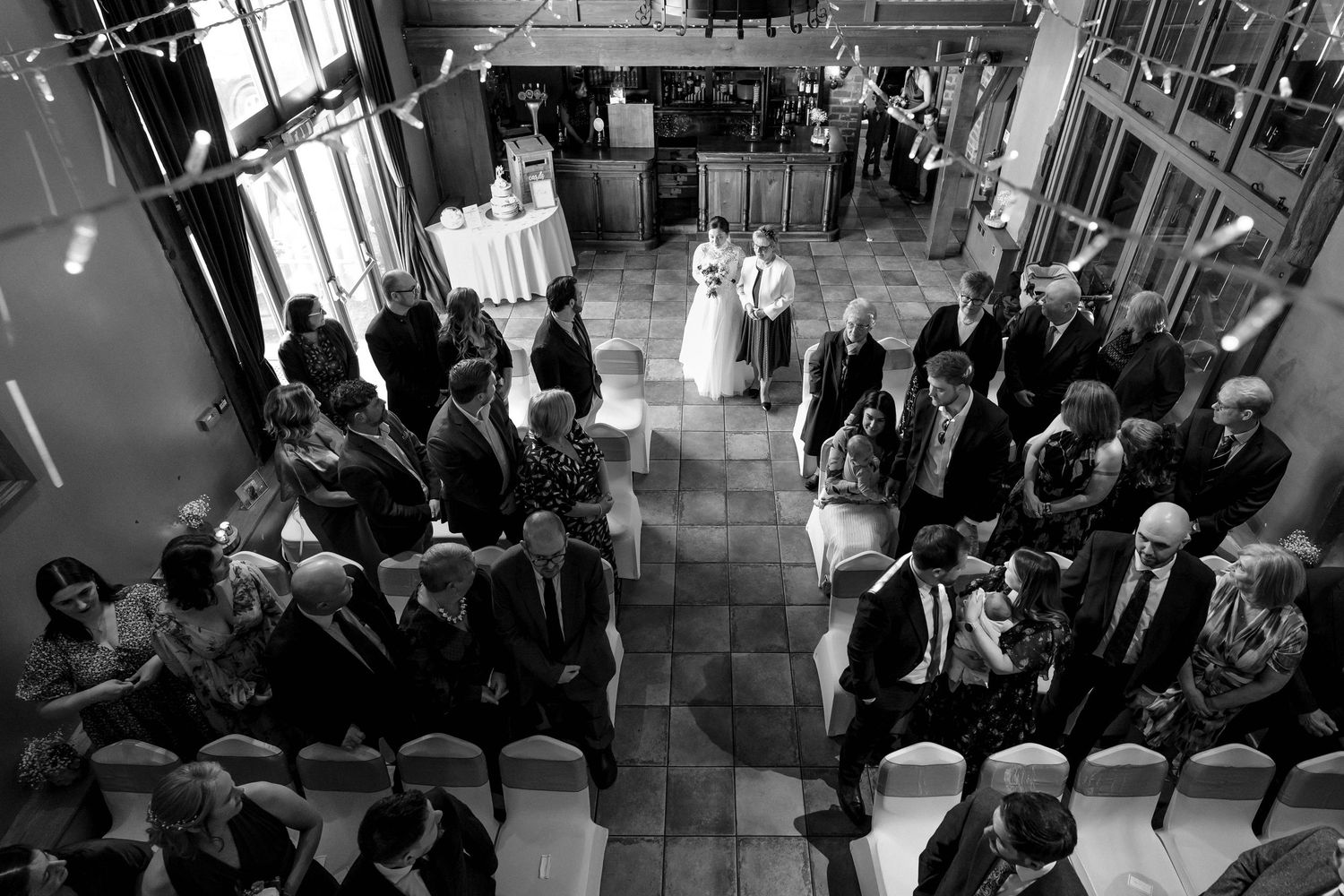 Black and white overhead view of a wedding ceremony with guests gathered in an elegant indoor venue.