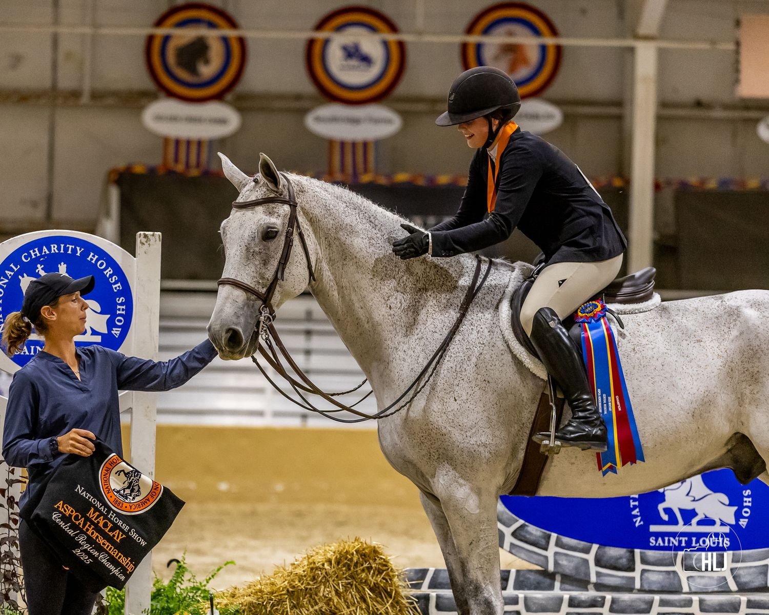 A dressage horse and rider competing in an arena with award ribbons displayed on the wall.