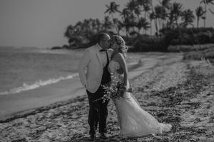 Black and white photo of a couple kissing on a tropical beach wedding, with palm trees and ocean in the background.
