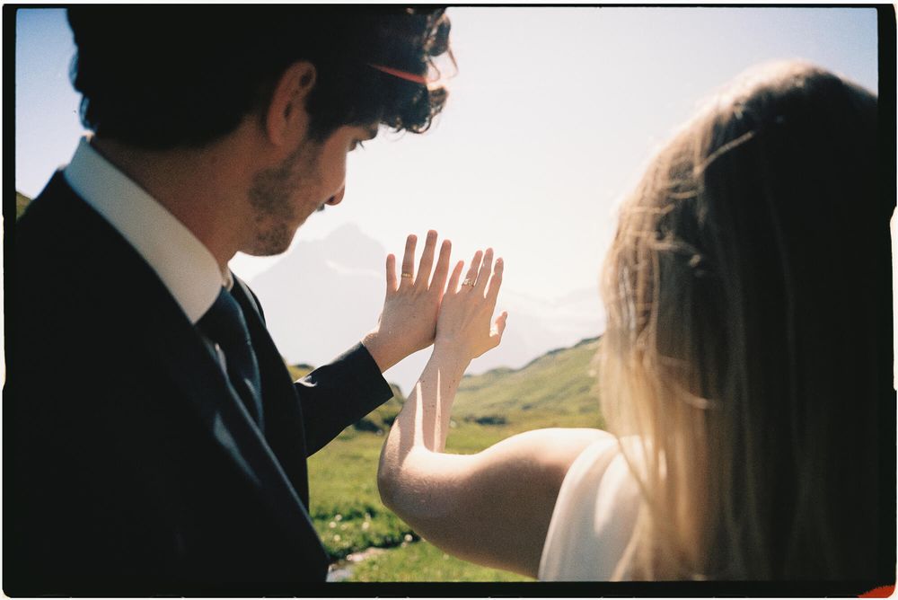 Bride and groom touching hands outdoors with scenic mountain landscape in background on wedding day.
