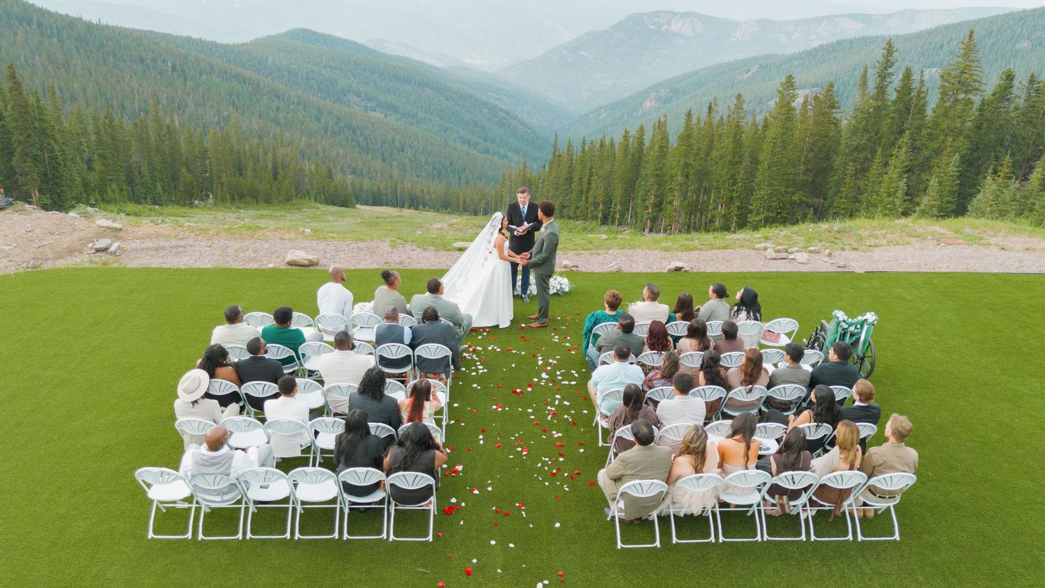 Aerial view of an outdoor wedding ceremony on a golf course with mountain and forest backdrop.