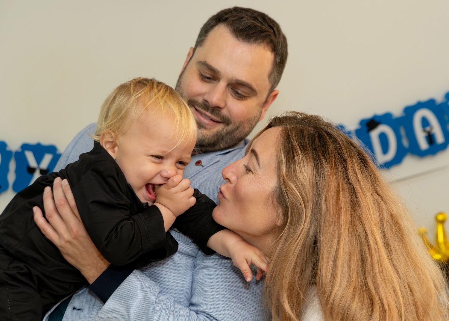 Happy family with parents smiling at laughing baby boy at a birthday party celebration.