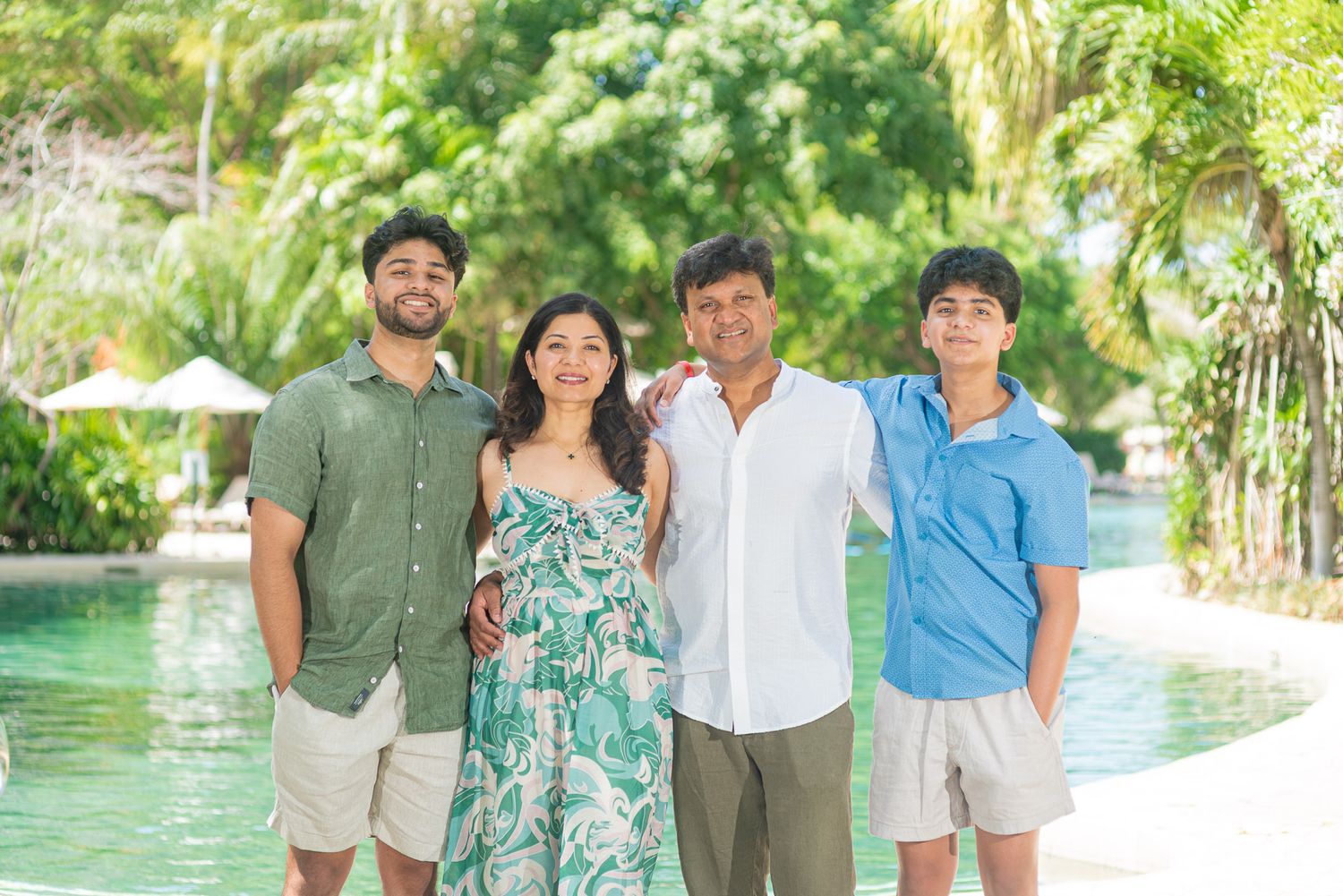 Family of four smiling together poolside surrounded by lush tropical greenery at a resort.