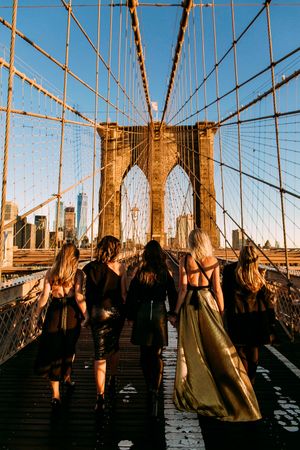 Group walking across Brooklyn Bridge during golden hour with Manhattan skyline in background.