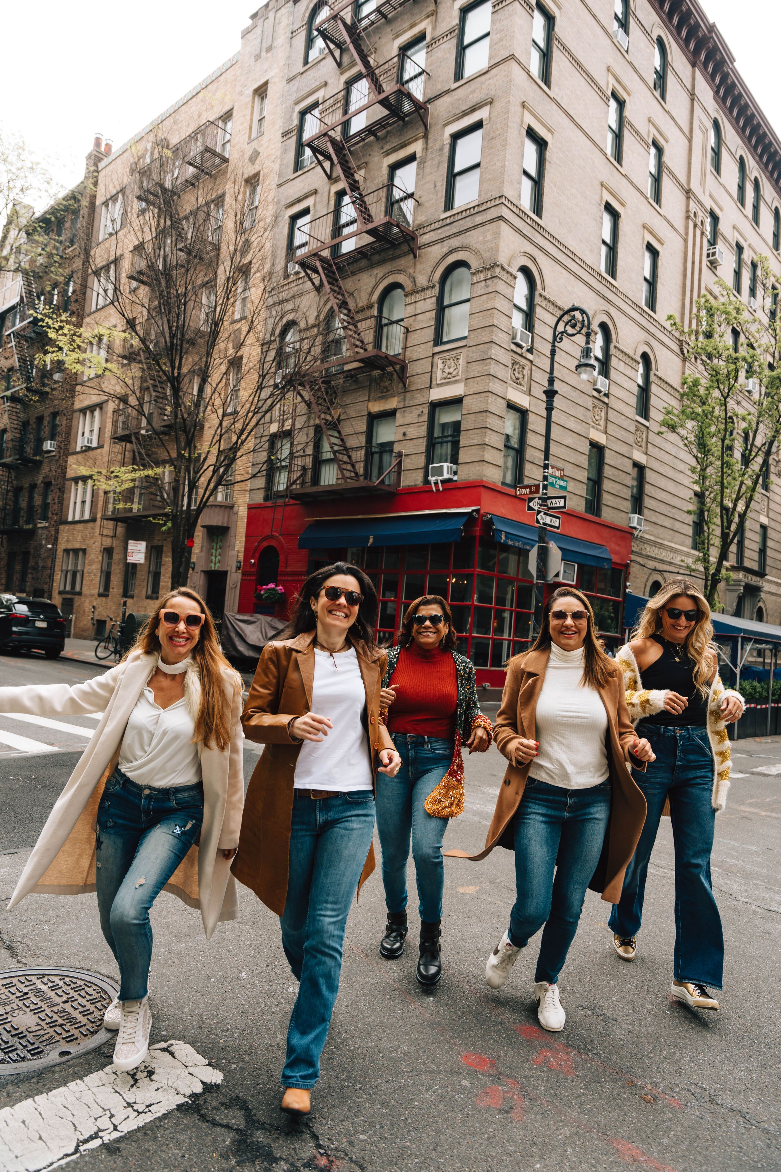 Group walking down NYC street with classic brownstone buildings and red bus in background.