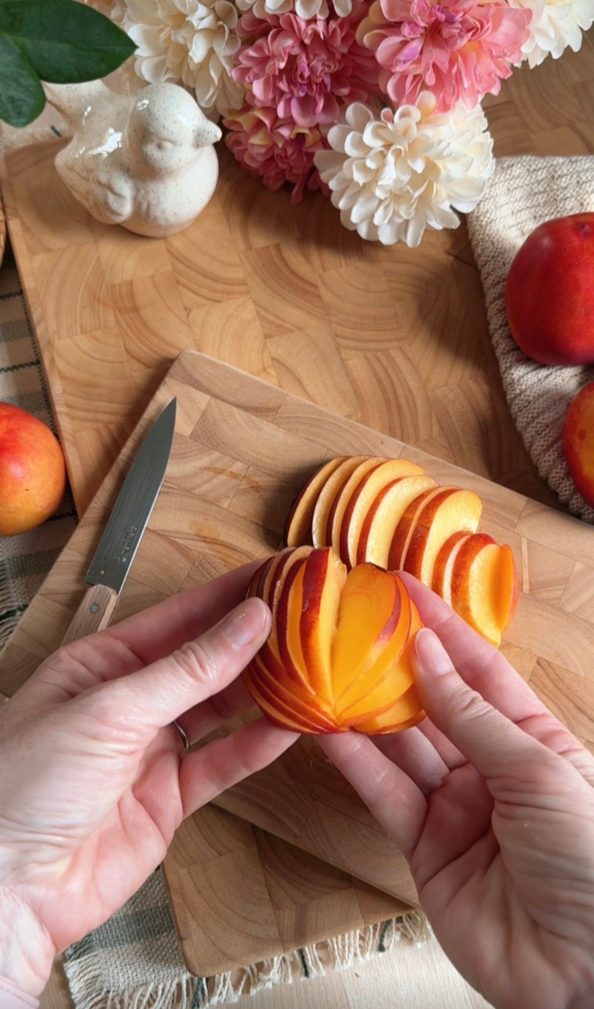 Sliced peaches arranged in overlapping rows in a parchment-lined loaf pan, ready for baking, with pink flowers in background.