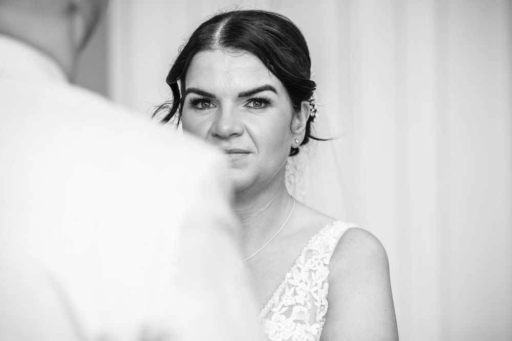 Black and white photo of a bride in lace wedding dress and veil gazing forward with an emotional expression.