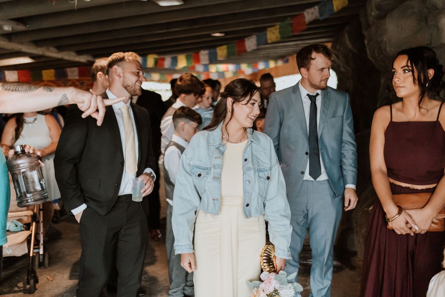 Wedding guests dancing and socializing at a rustic indoor reception venue decorated with colorful bunting flags.