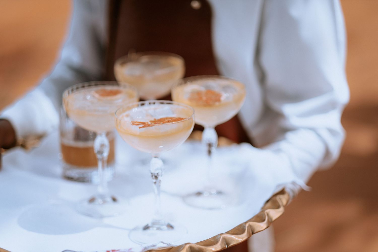 Waiter serving elegant champagne coupe cocktails on a tray at an upscale outdoor event.