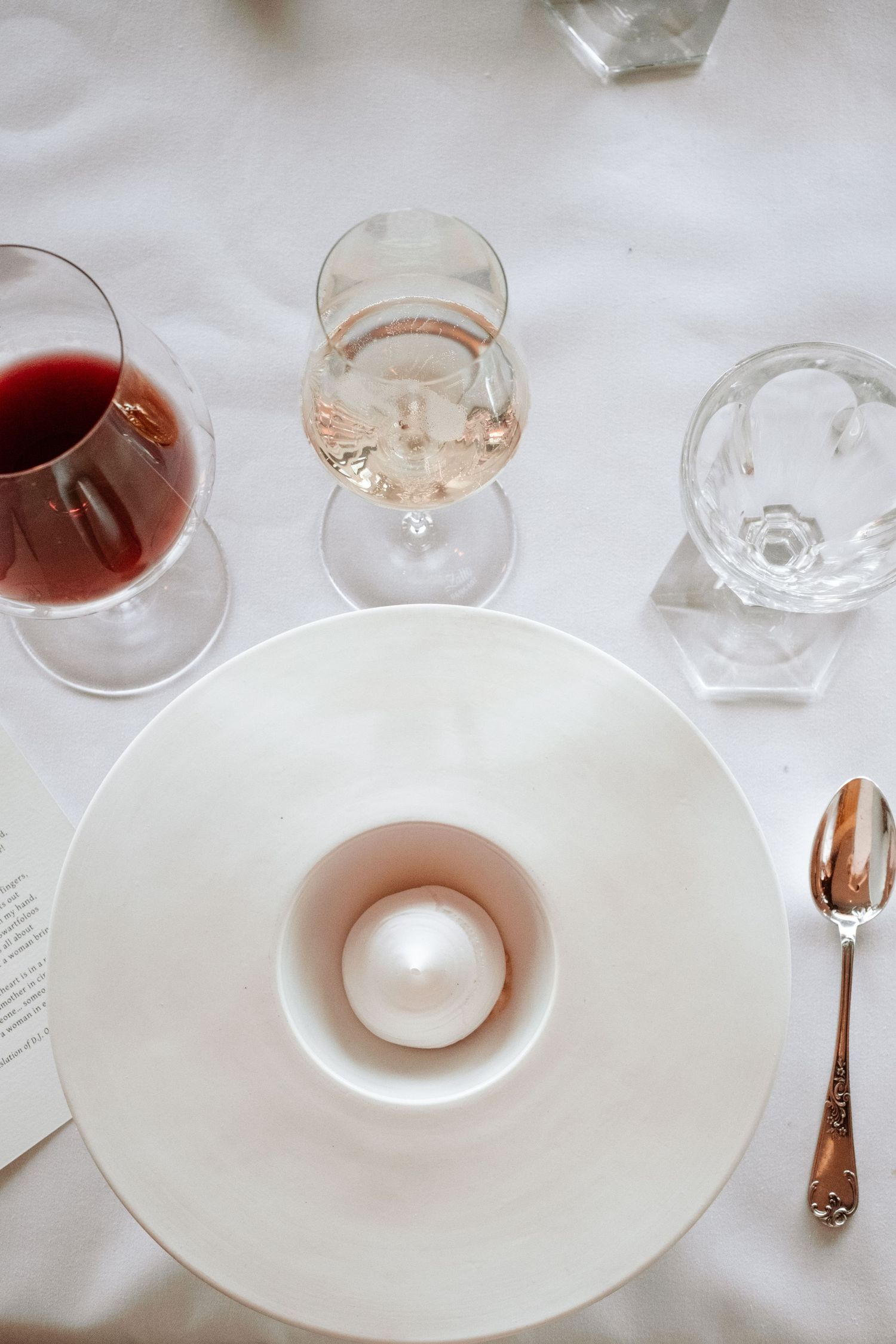Elegant fine dining table setting with white plate, pearl garnish, rose wine, red wine glasses, and silver spoon.