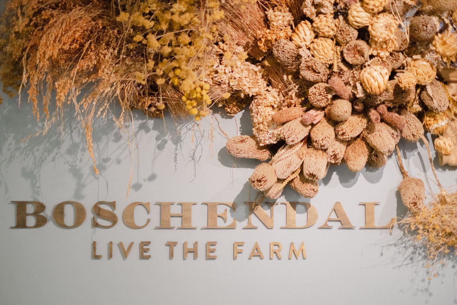Boschendal Live The Farm sign decorated with dried botanical arrangements in warm earth tones.