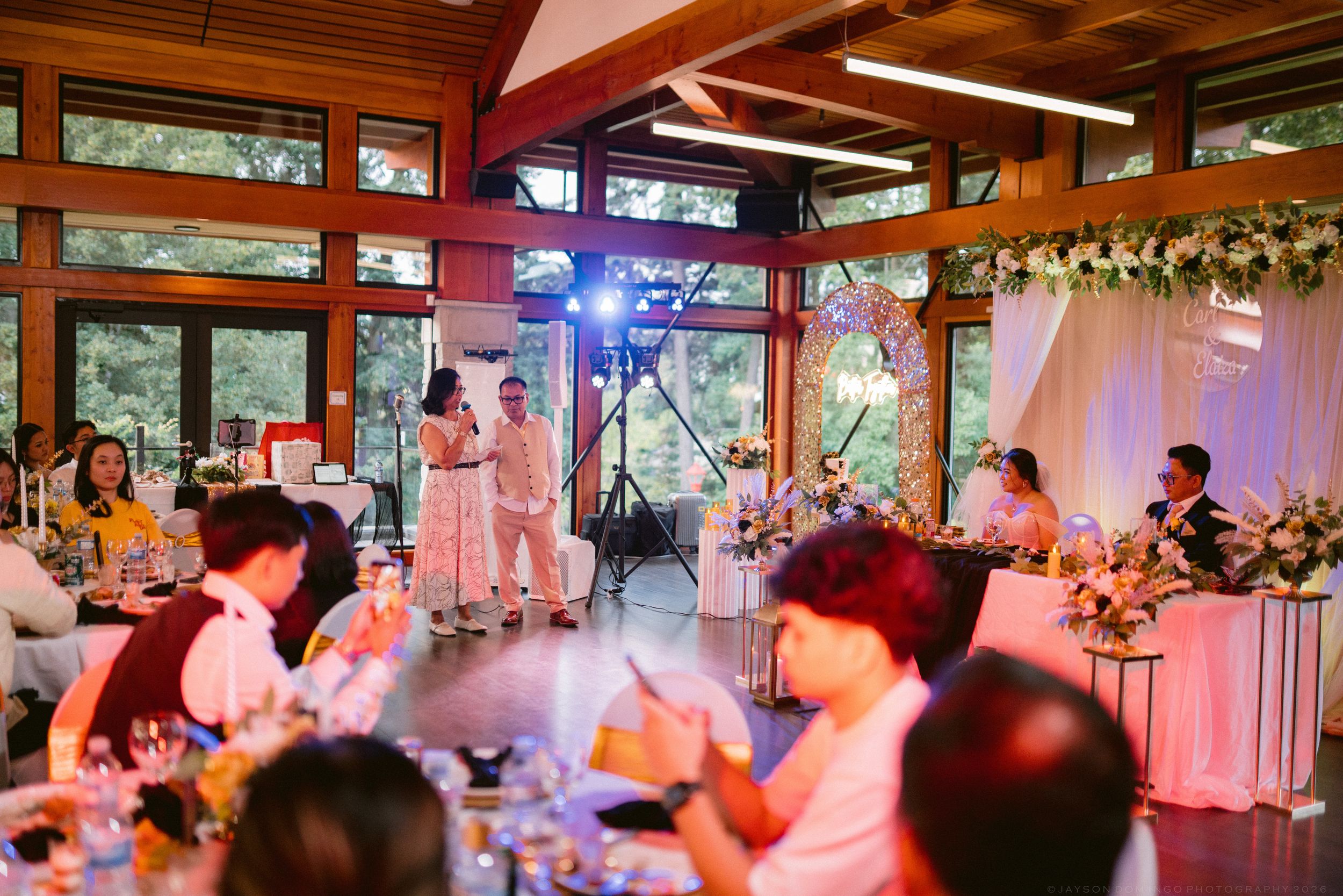 Guests enjoy a wedding reception with live entertainment in a wood-paneled venue with large windows.