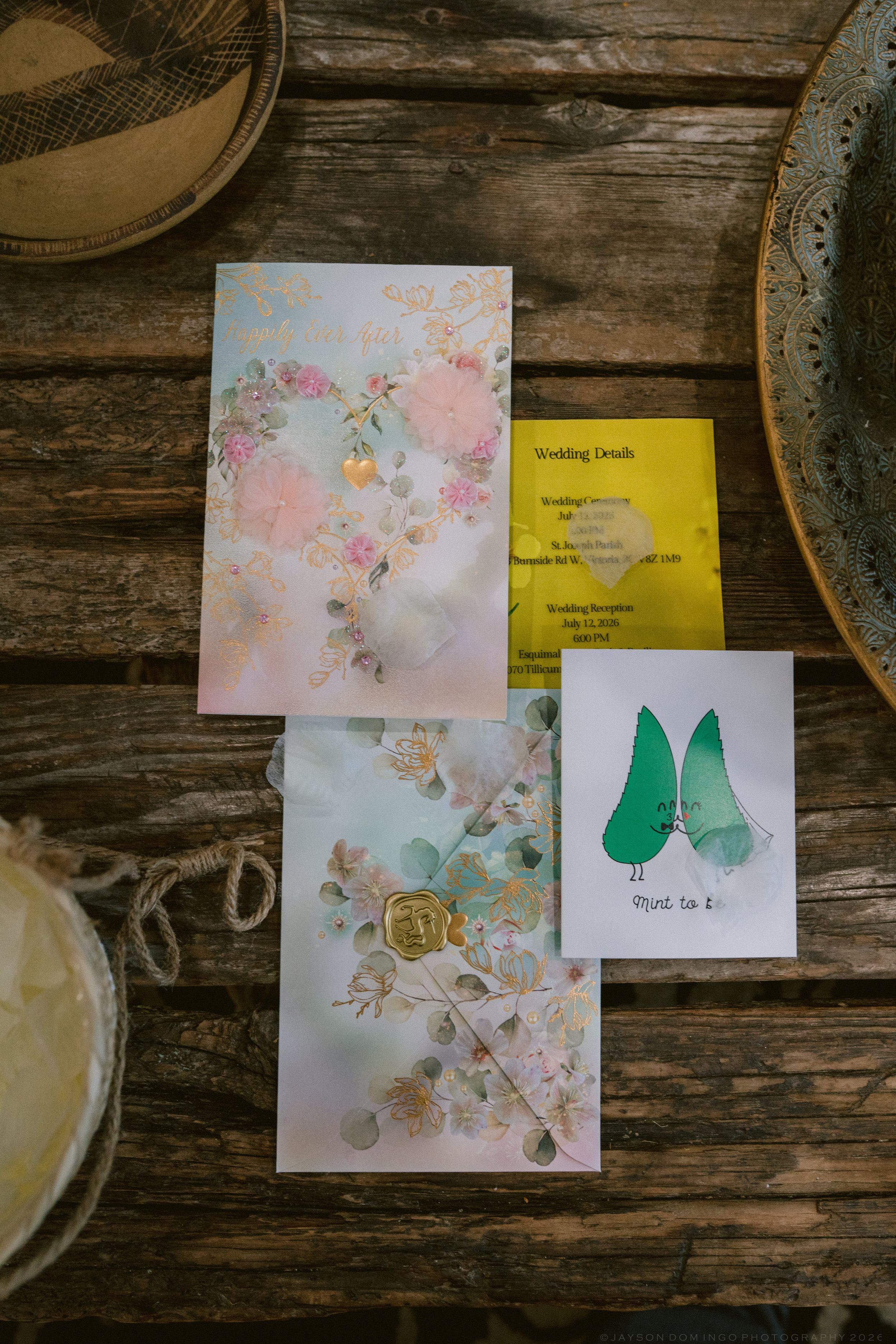 Rustic wedding stationery flat lay on wood table featuring floral invitations, yellow details card, and cute avocado couple card.