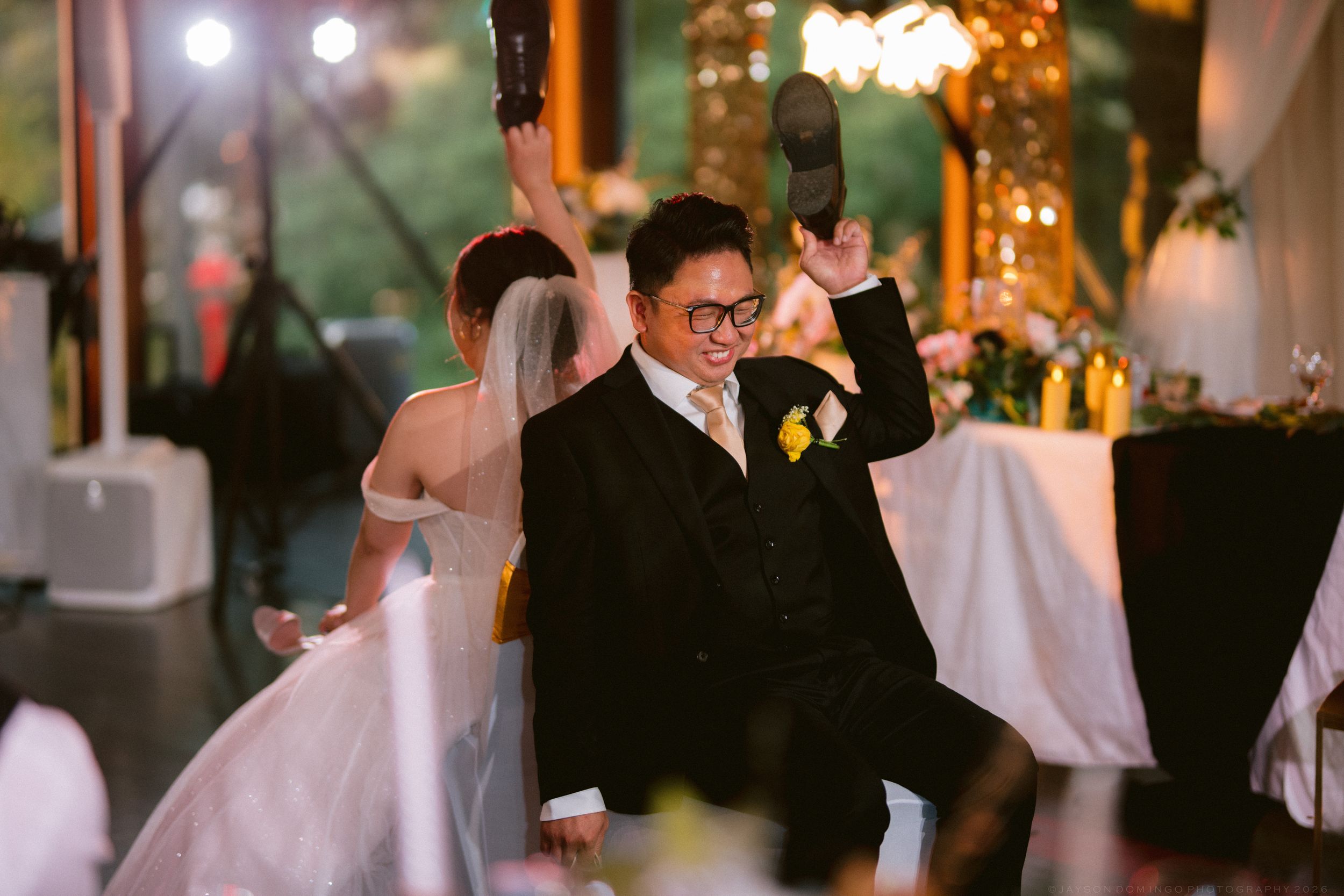 A groom celebrates energetically on the dance floor at his wedding reception in a decorated venue.
