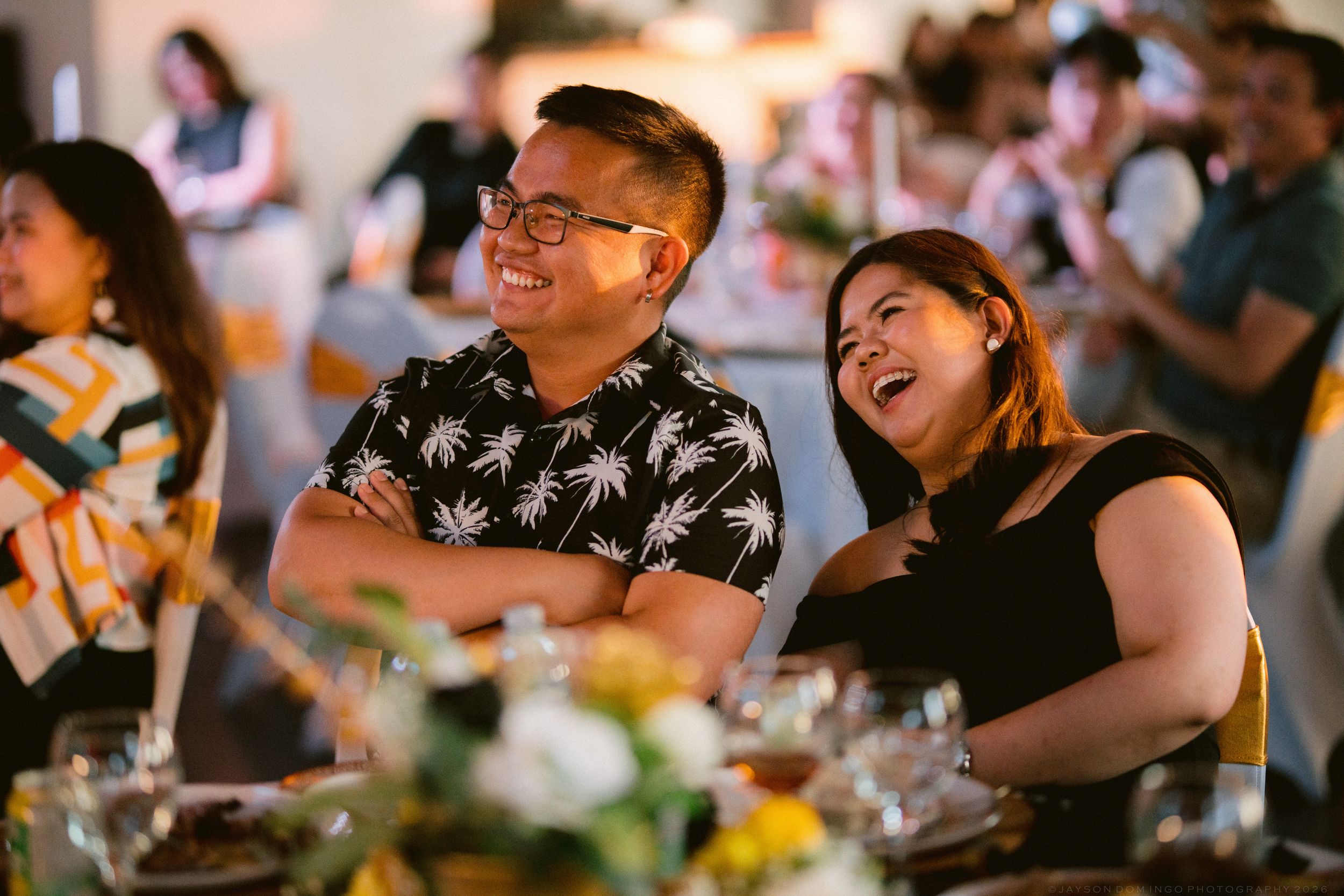 A smiling couple laughs together while seated at a wedding reception dinner table.