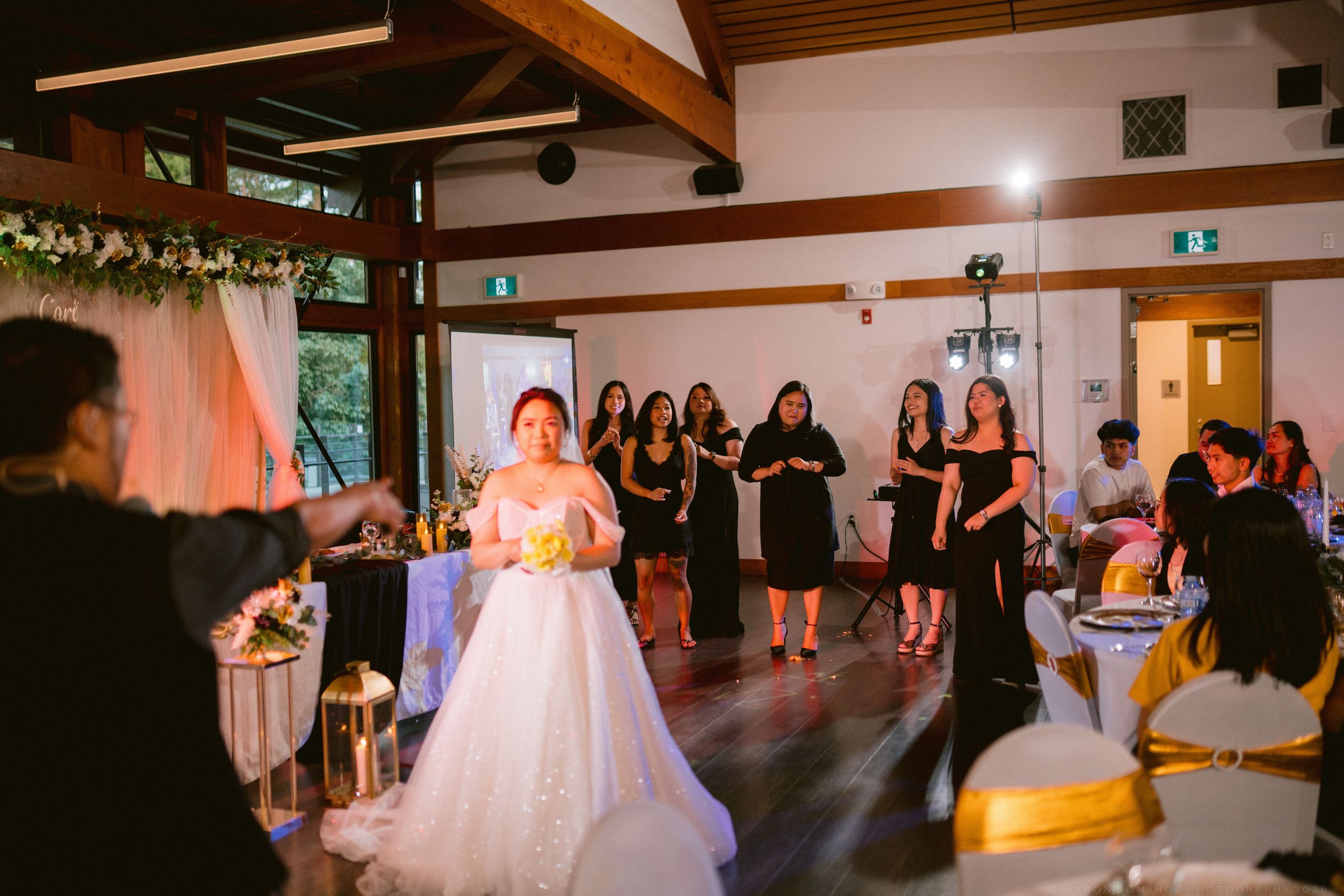 A bride in a white ball gown prepares to toss her bouquet to a group of women at the reception.