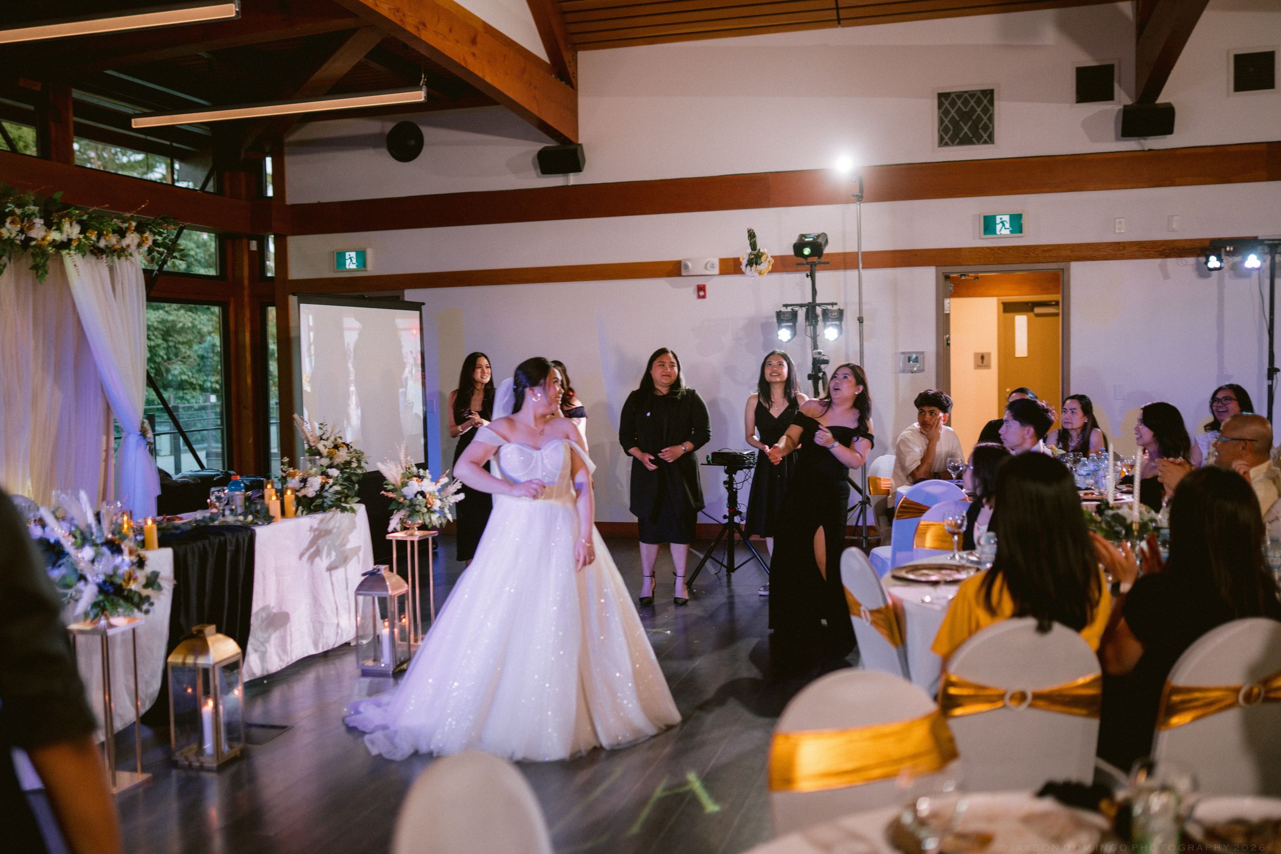 A bride in a white gown stands on the dance floor surrounded by guests at a wedding reception.