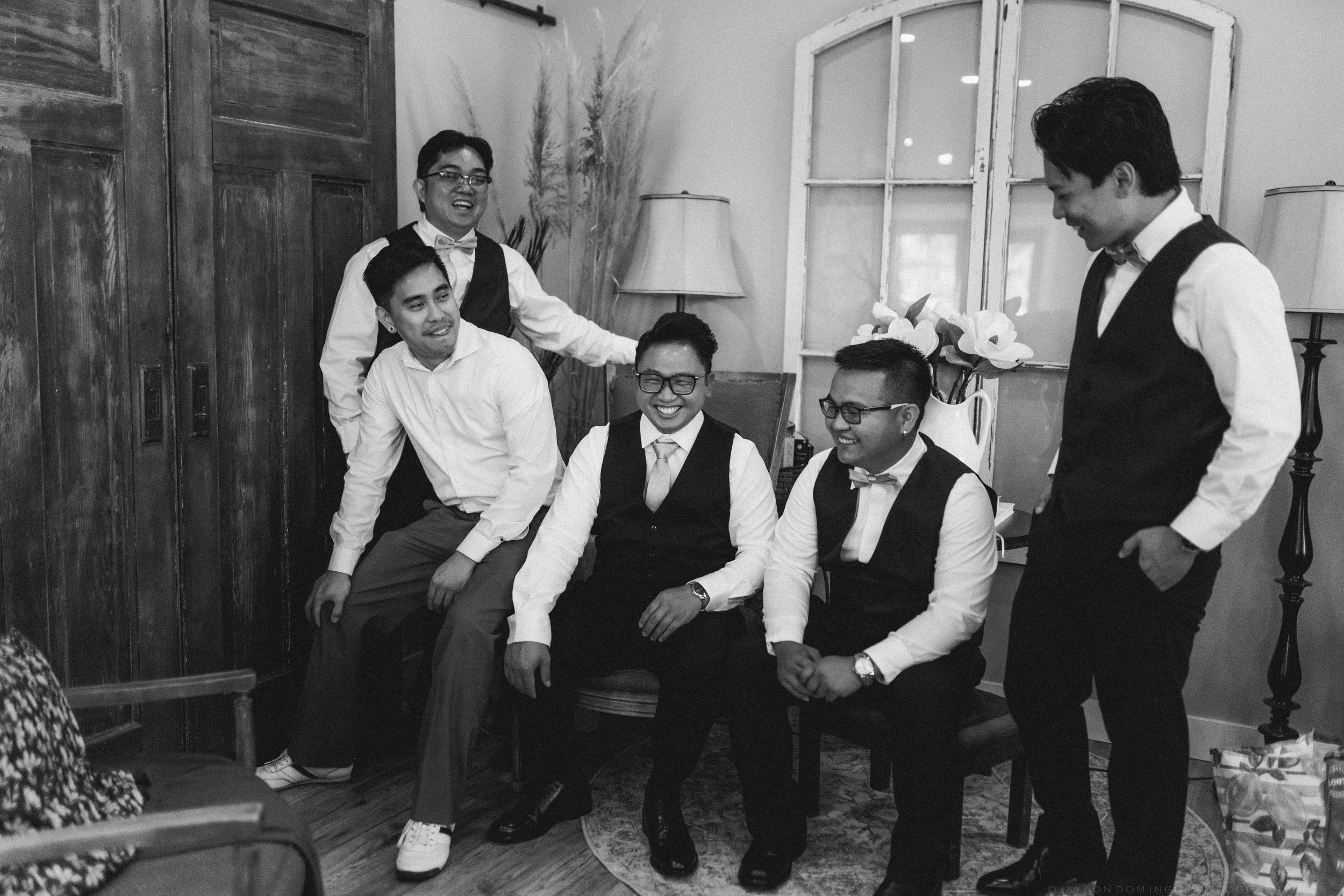 Black and white photo of five groomsmen laughing and relaxing together before wedding ceremony.