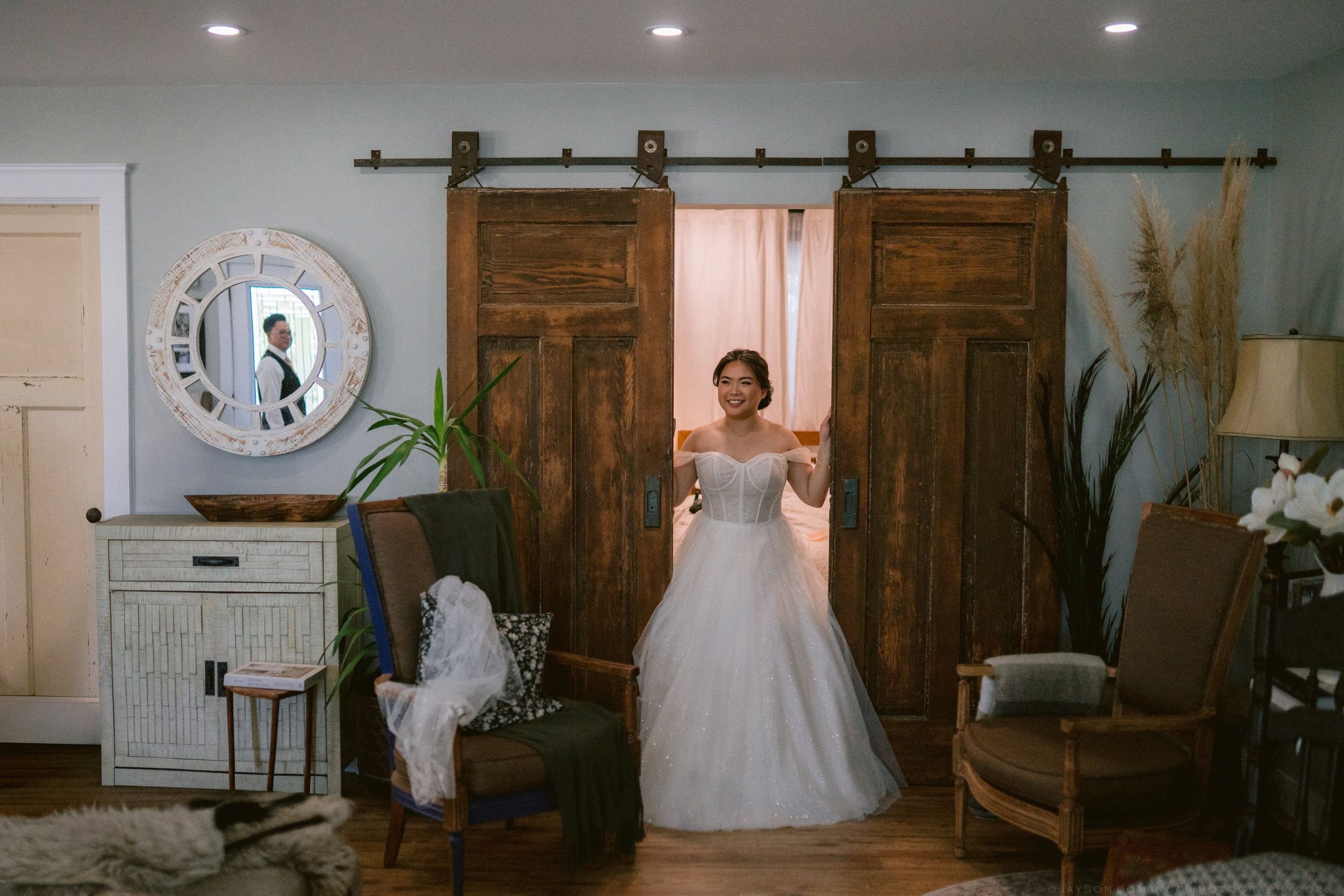 Bride in a white ball gown wedding dress standing in front of rustic wooden barn doors in an elegant indoor venue.
