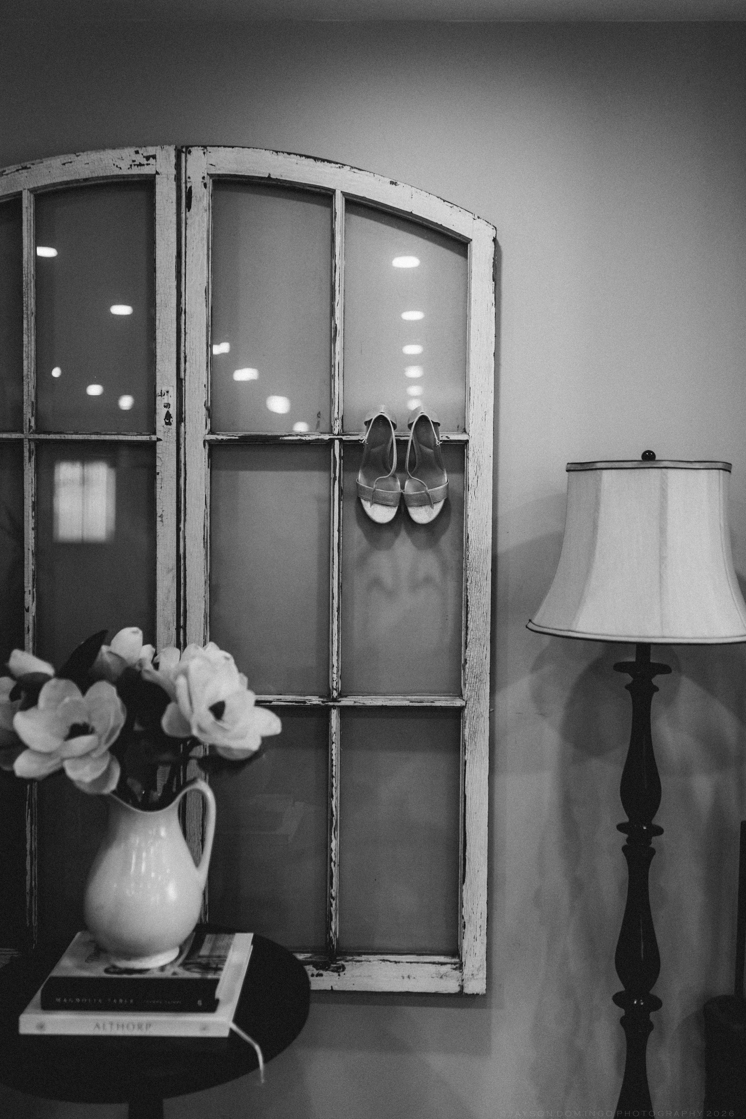 Black and white photo of bridal heels displayed in vintage arched window frame with flowers.