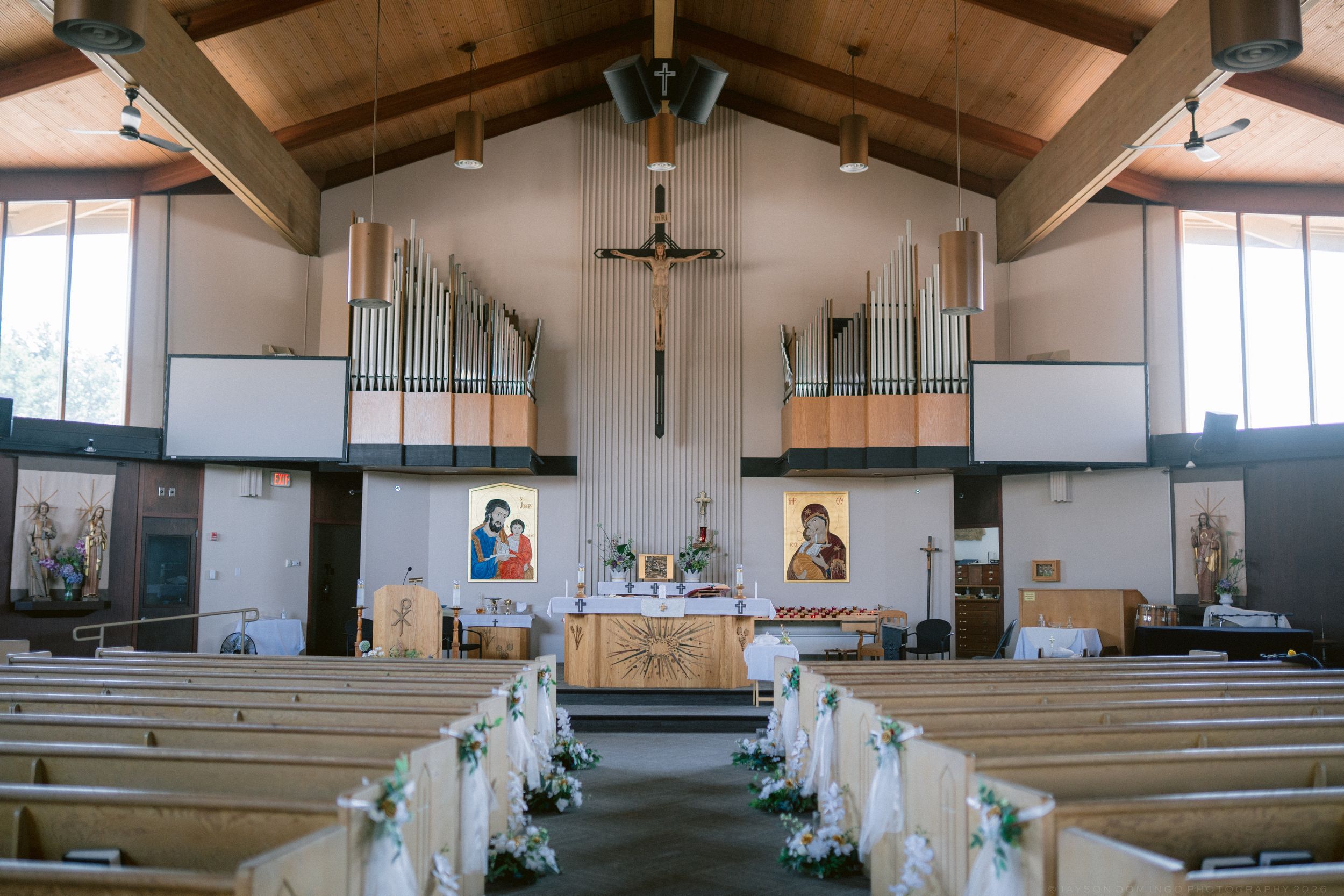 Elegant Catholic church interior decorated with white floral arrangements along pews for wedding.