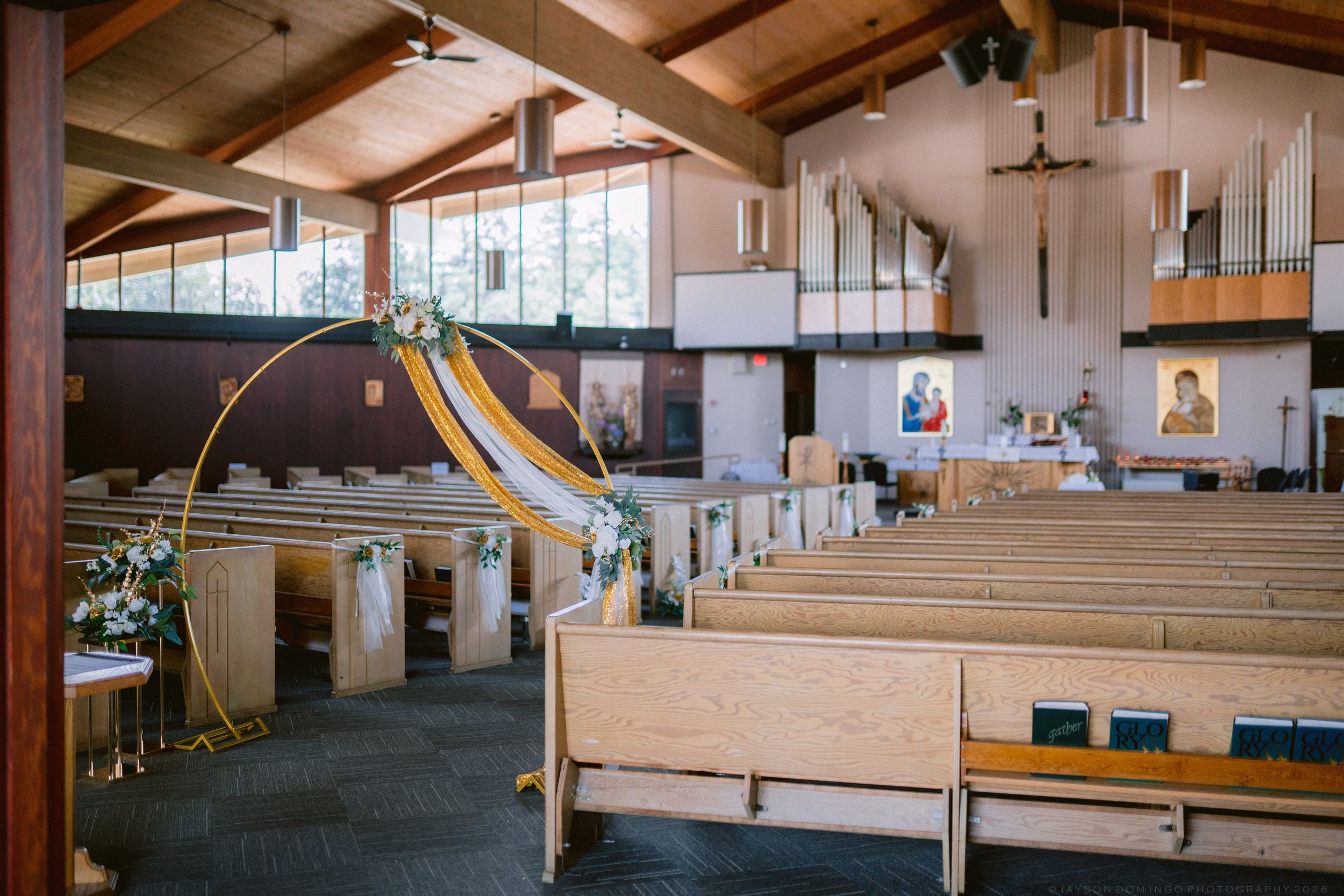 Church interior with wooden pews, floral arch, and altar decorated for a wedding ceremony.