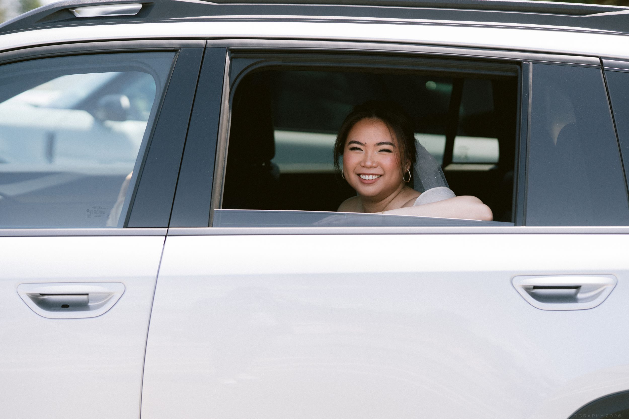 Smiling woman looking out the window of a white SUV on a sunny day.