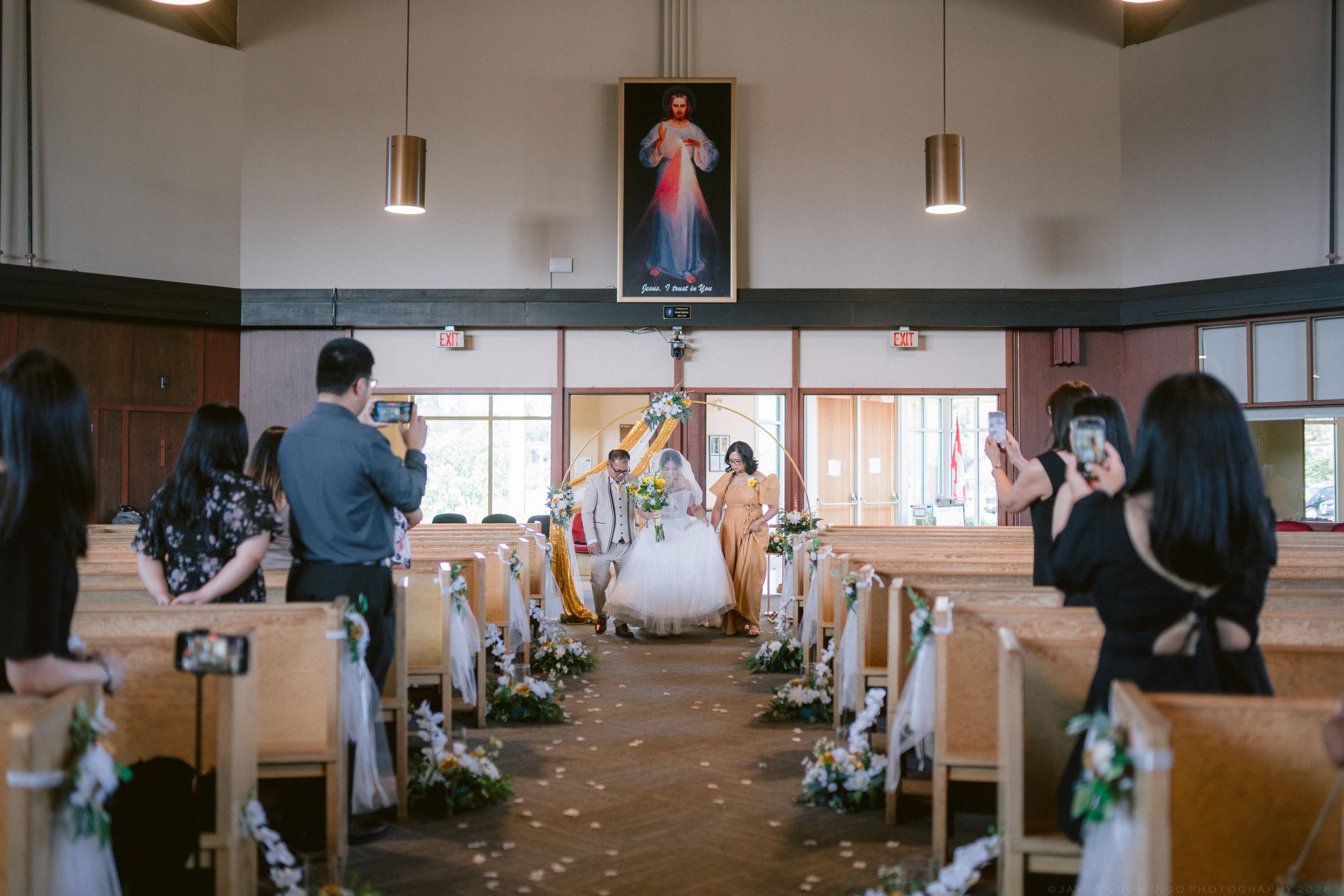 Wedding ceremony in a church with couple walking down the aisle as guests photograph the moment.