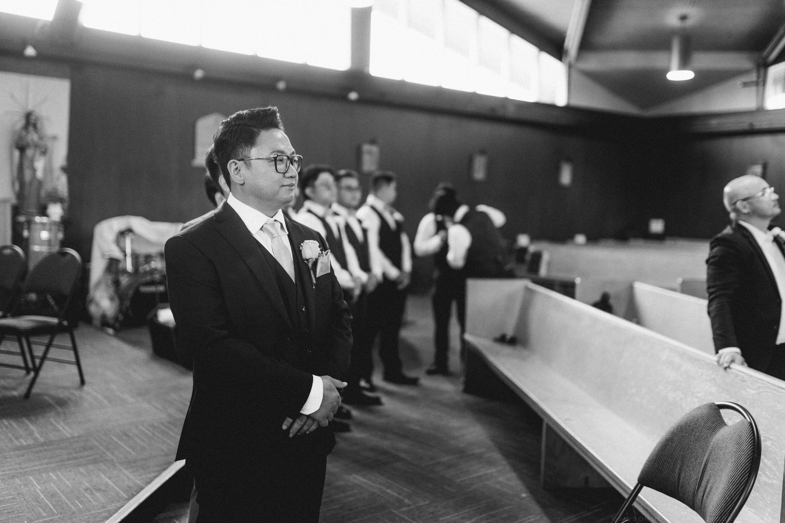 Black and white photo of a groom standing at the altar awaiting his bride in a church.