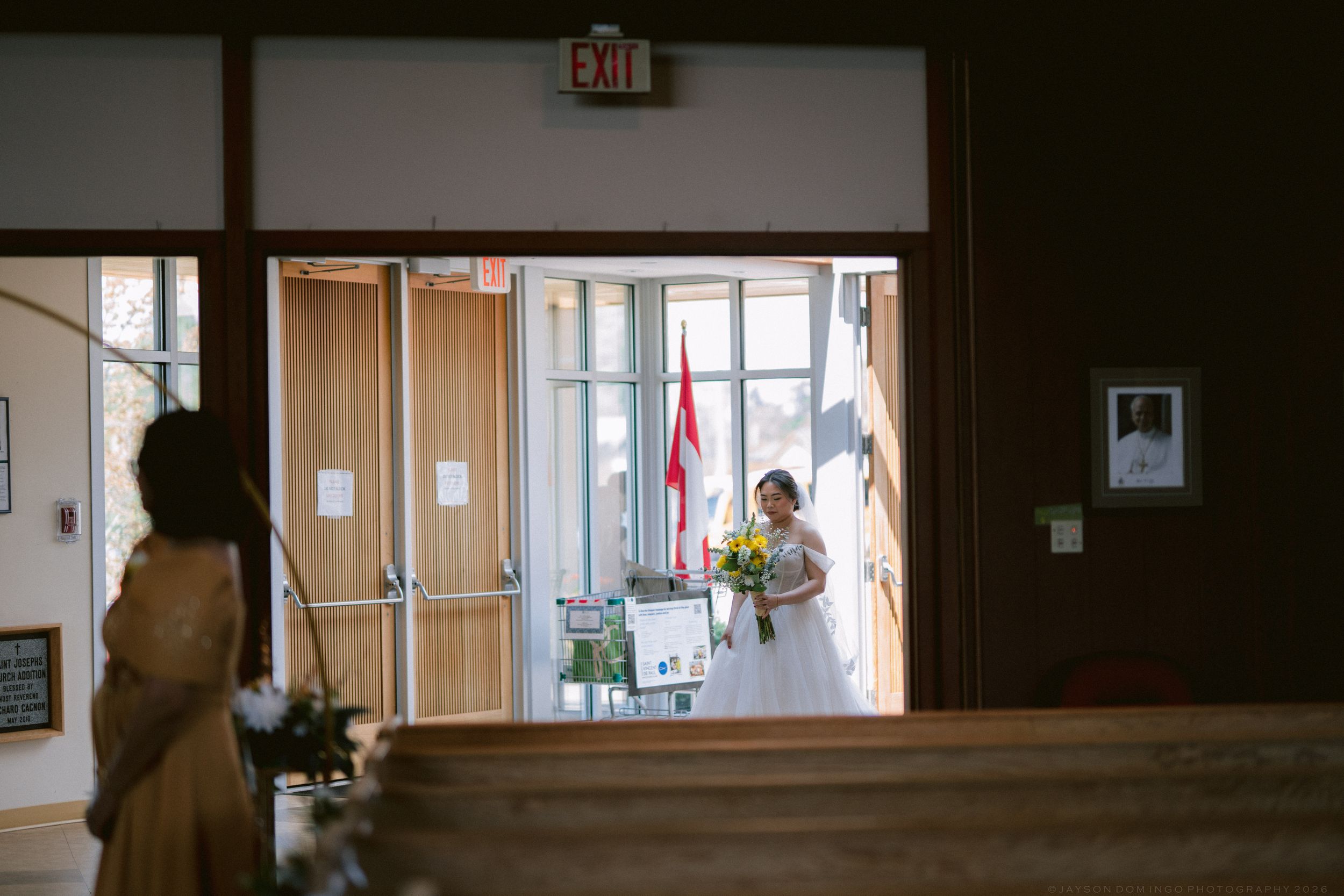 A bridesmaid holding yellow flowers stands in the church doorway preparing to walk down the aisle.