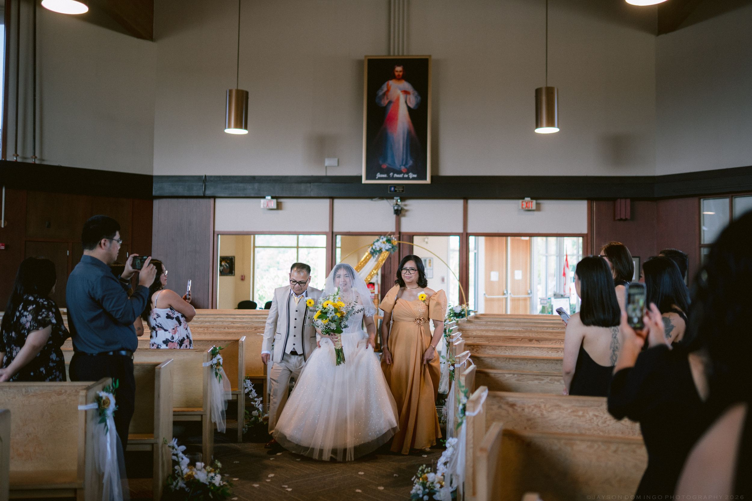 Bride and groom walk down church aisle after Catholic wedding ceremony.