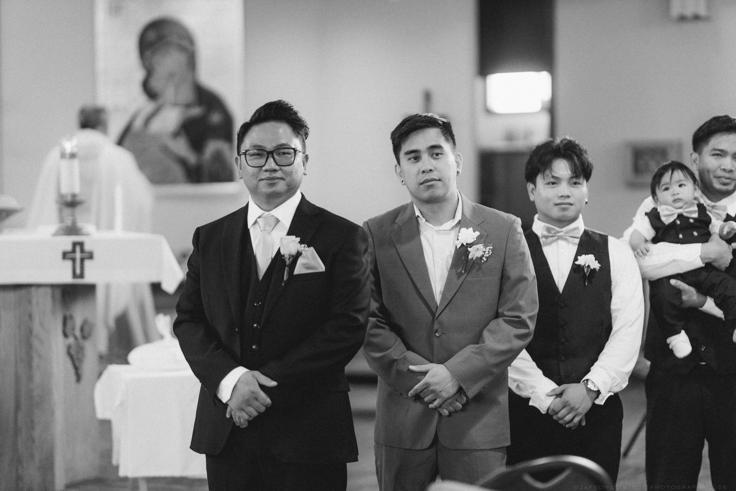 A groom and groomsmen stand at the altar in a church waiting for the ceremony to begin.