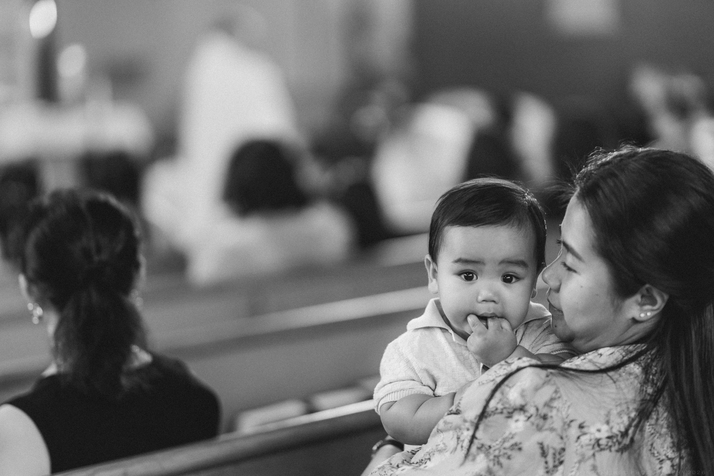 Mother holds adorable baby during wedding ceremony in black and white photo.