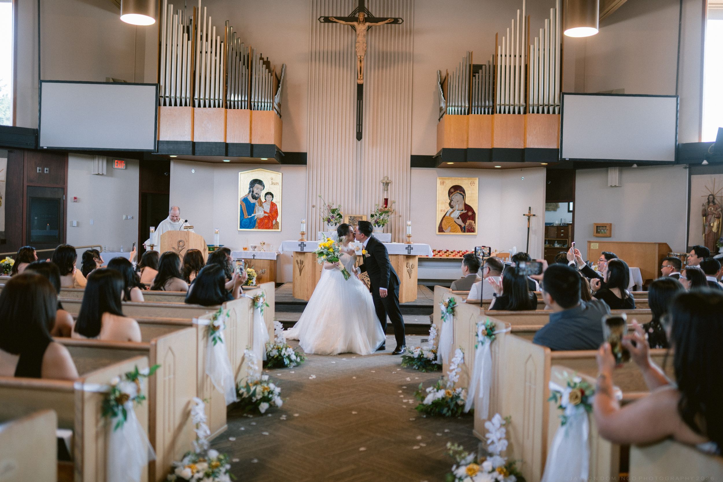 Wedding ceremony in a decorated church with guests seated in pews as couple stands at the altar.