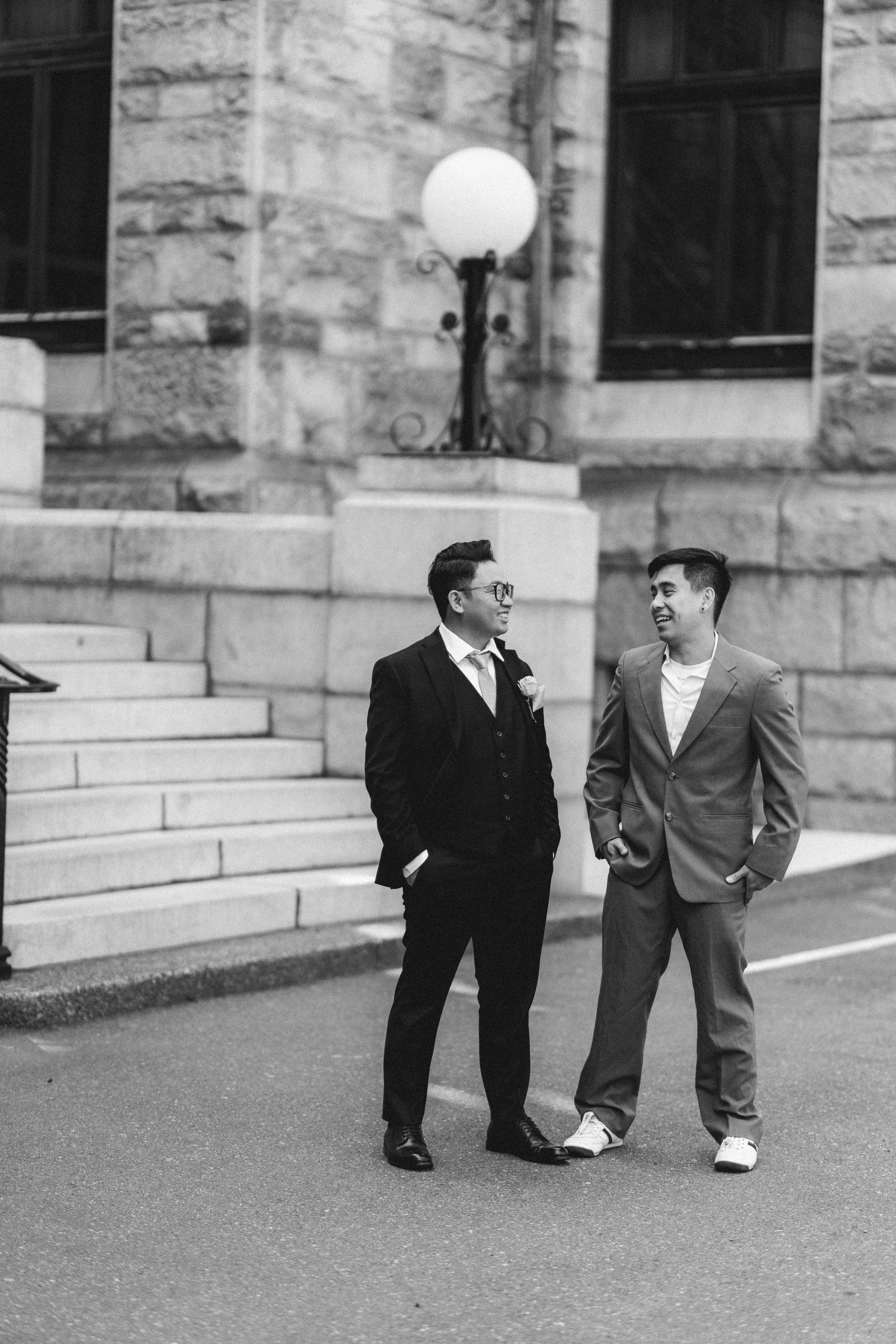 Black and white photo of two men in suits conversing outside a historic stone building.