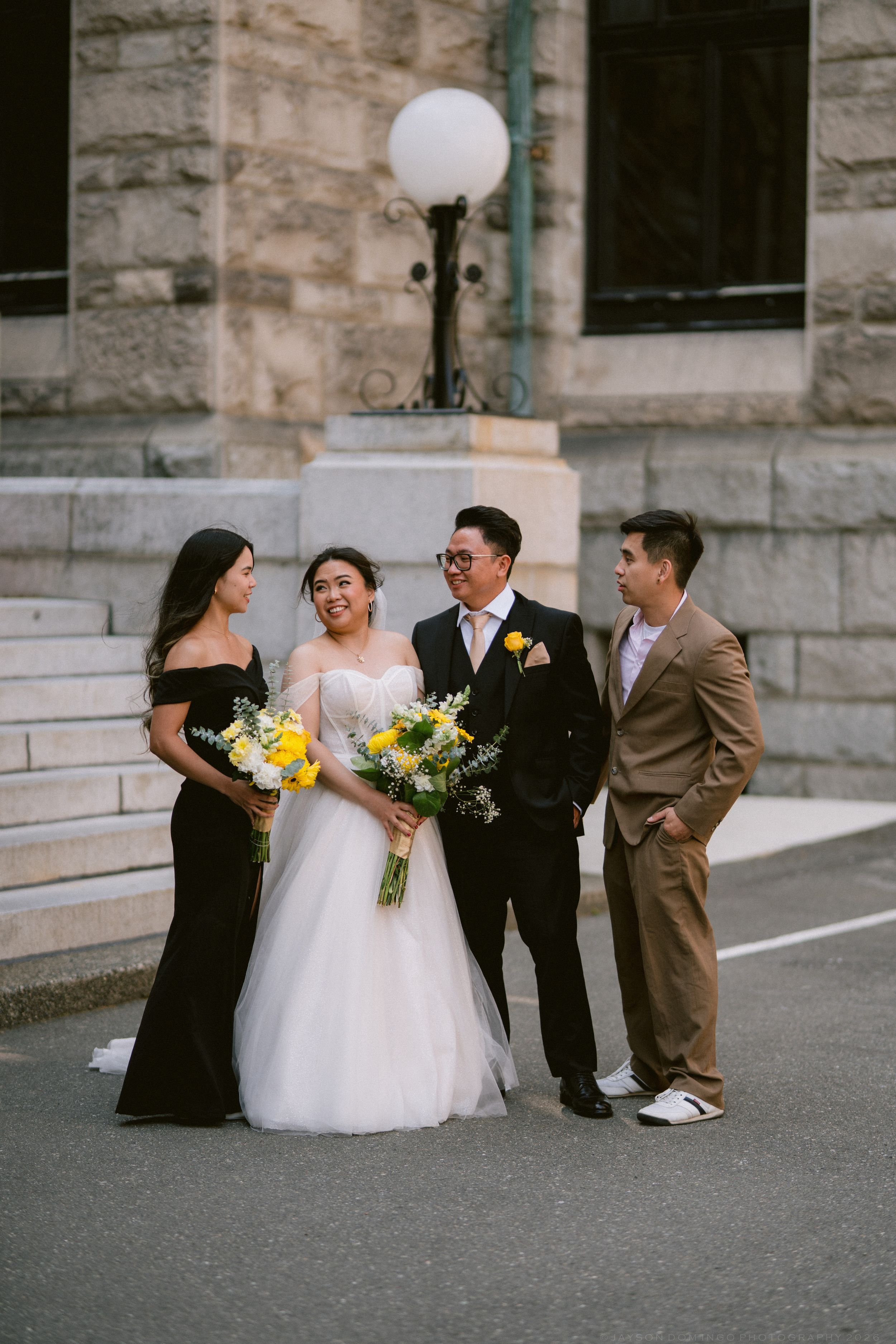 Wedding party of four poses and laughs outside a historic stone building with globe lamp post.