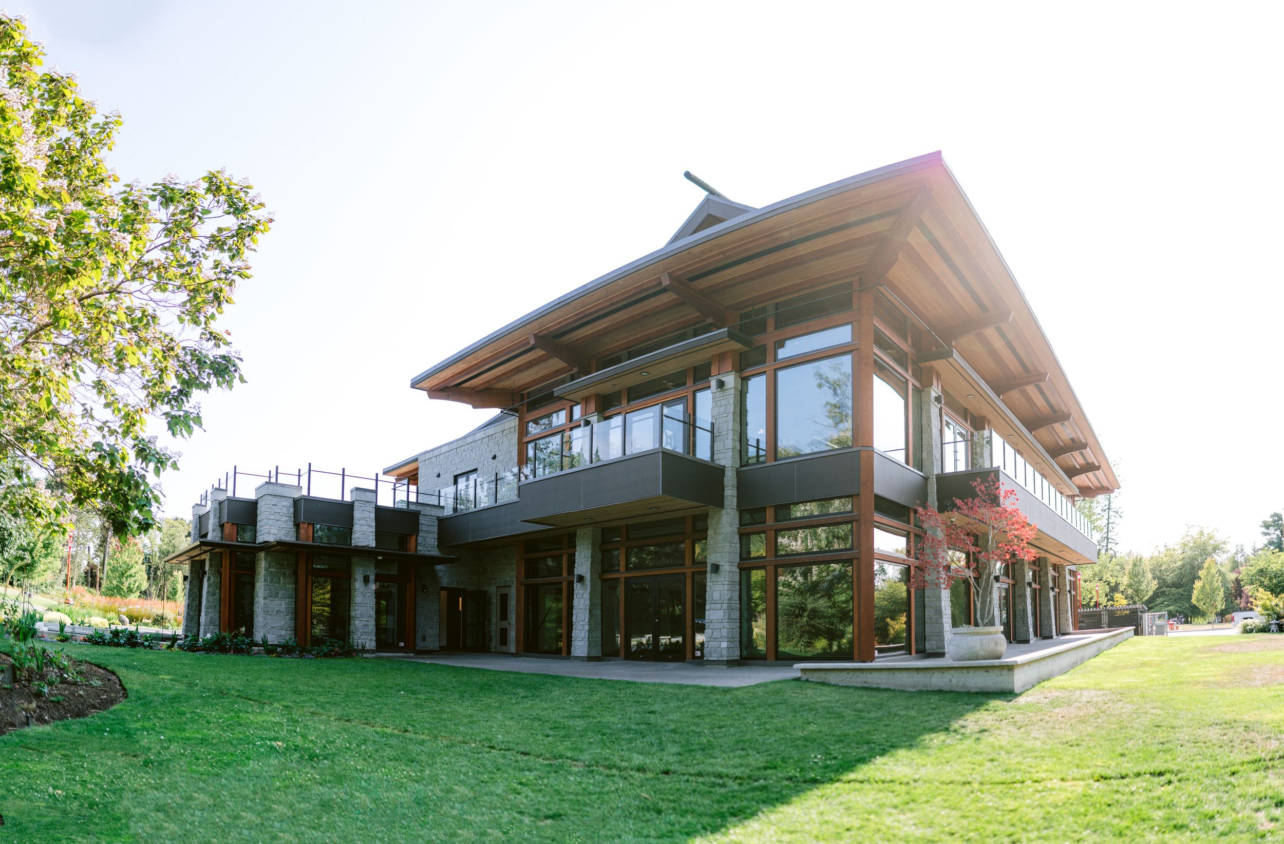 Modern architectural venue with wooden beams, large glass windows, and manicured green lawn on a sunny day.