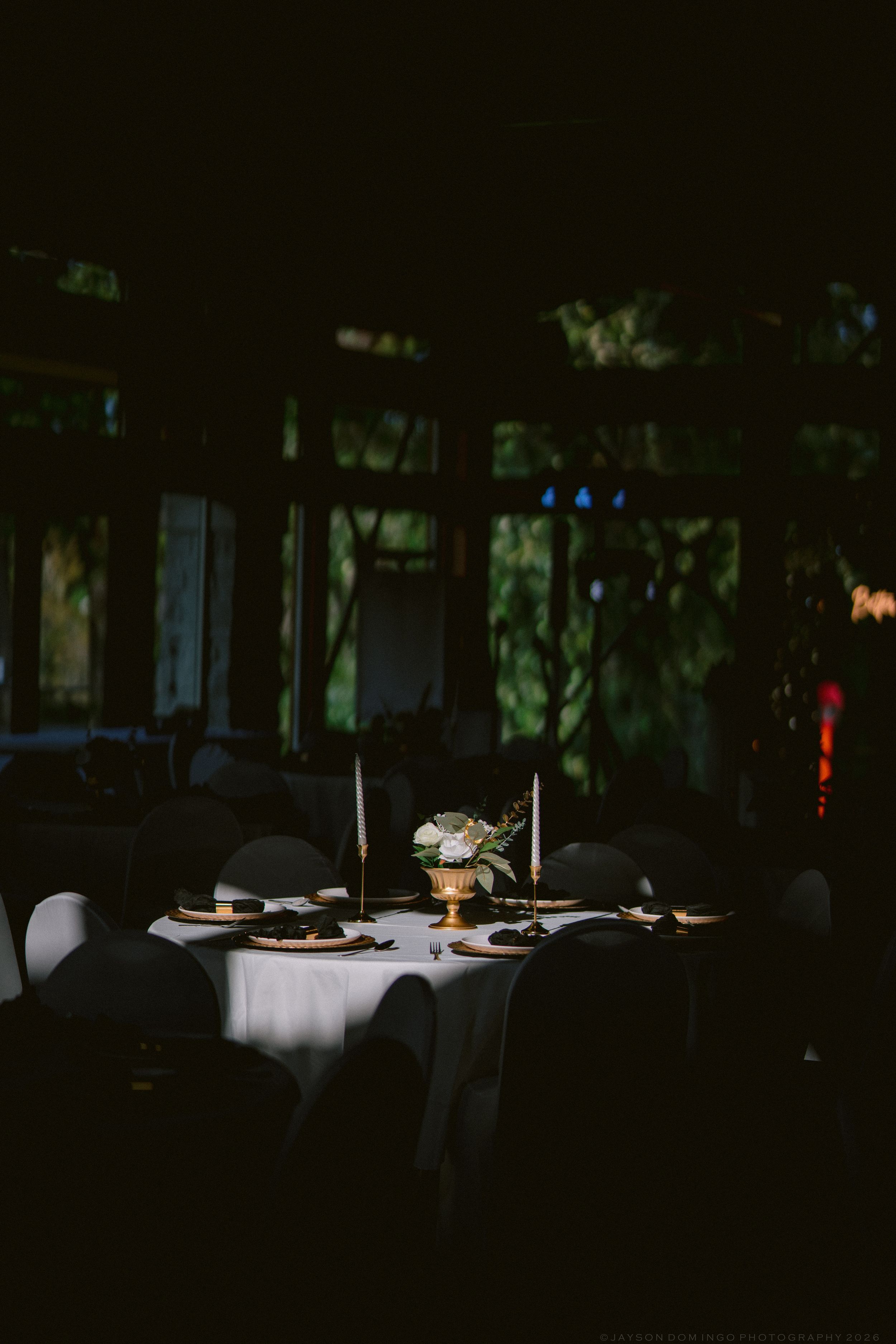 Elegantly set round wedding reception table with candles and floral centerpiece in dimly lit venue.