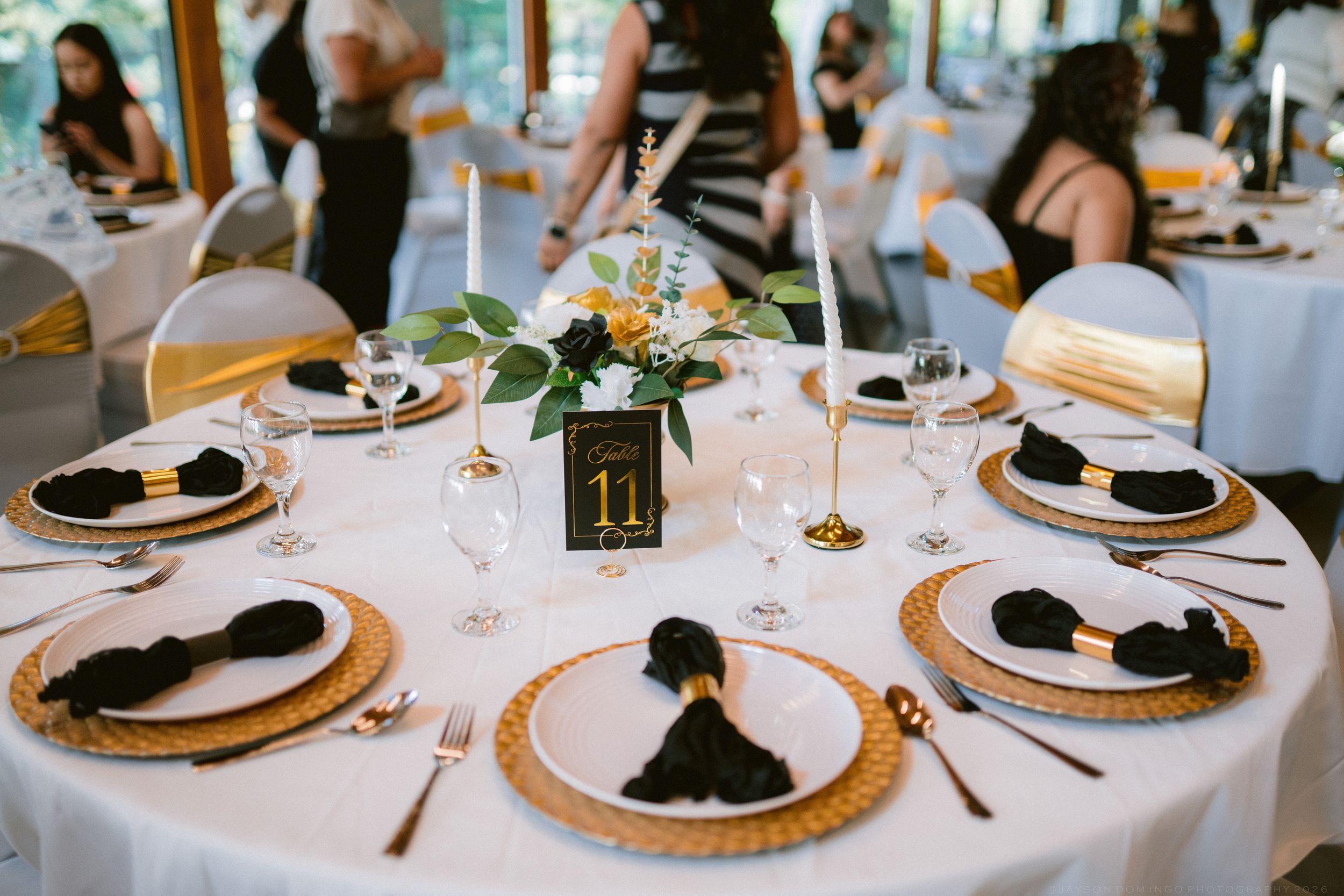 Elegant wedding reception table with gold charger plates, black napkins, and floral centerpiece.