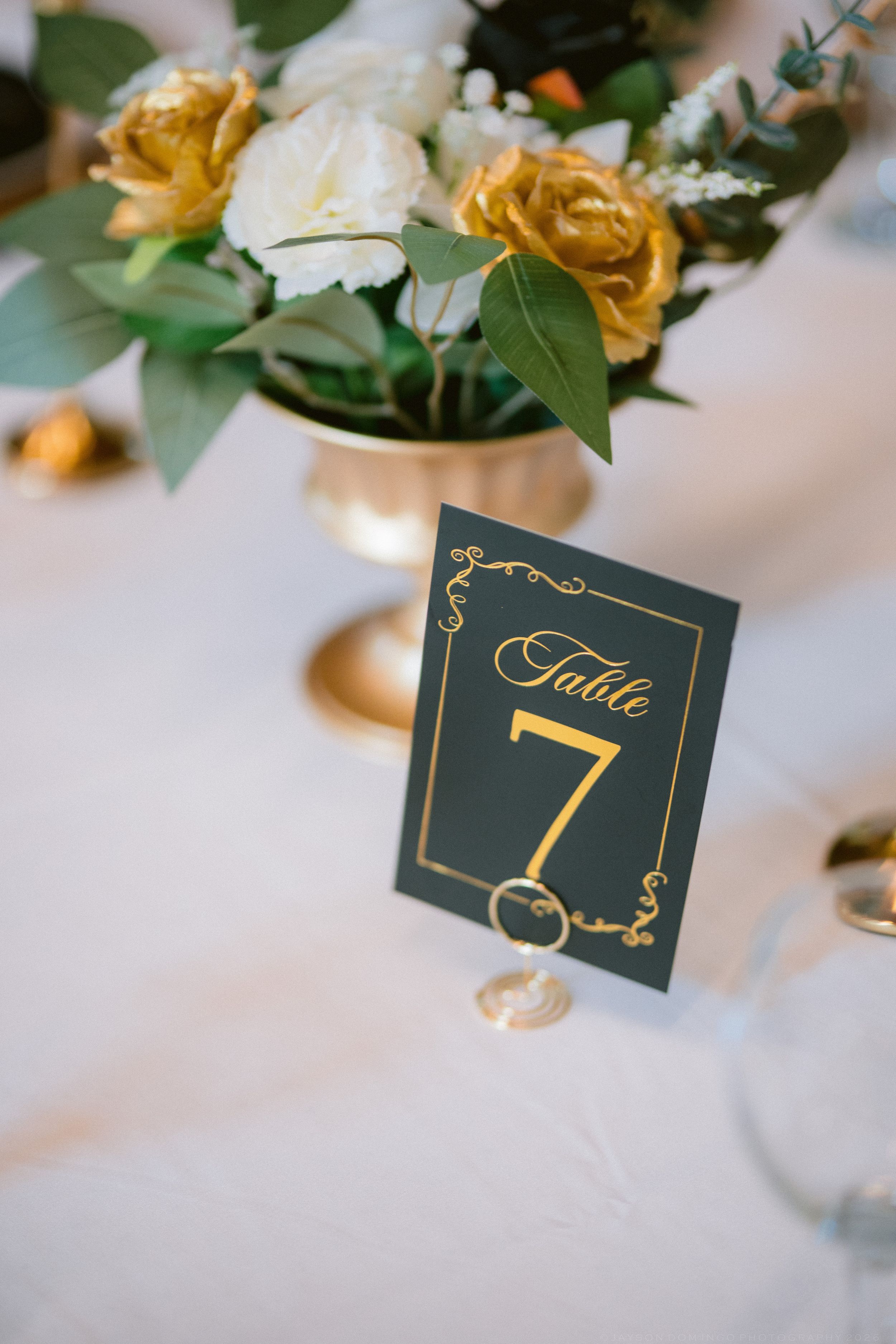 Dark green and gold Table 7 number card with white and gold rose floral centerpiece.