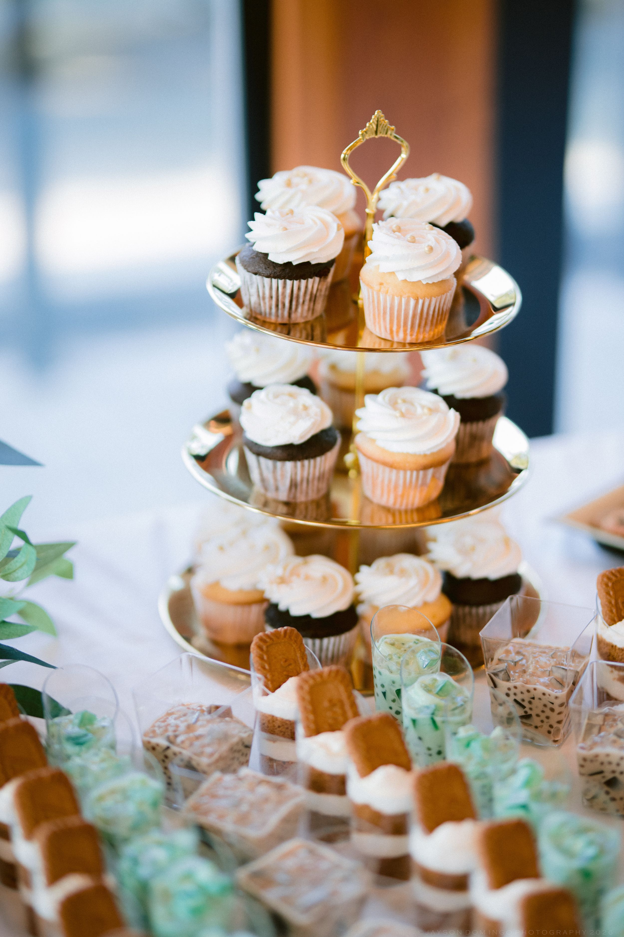 A three-tiered gold dessert stand displays assorted cupcakes and sweet treats at a wedding reception.
