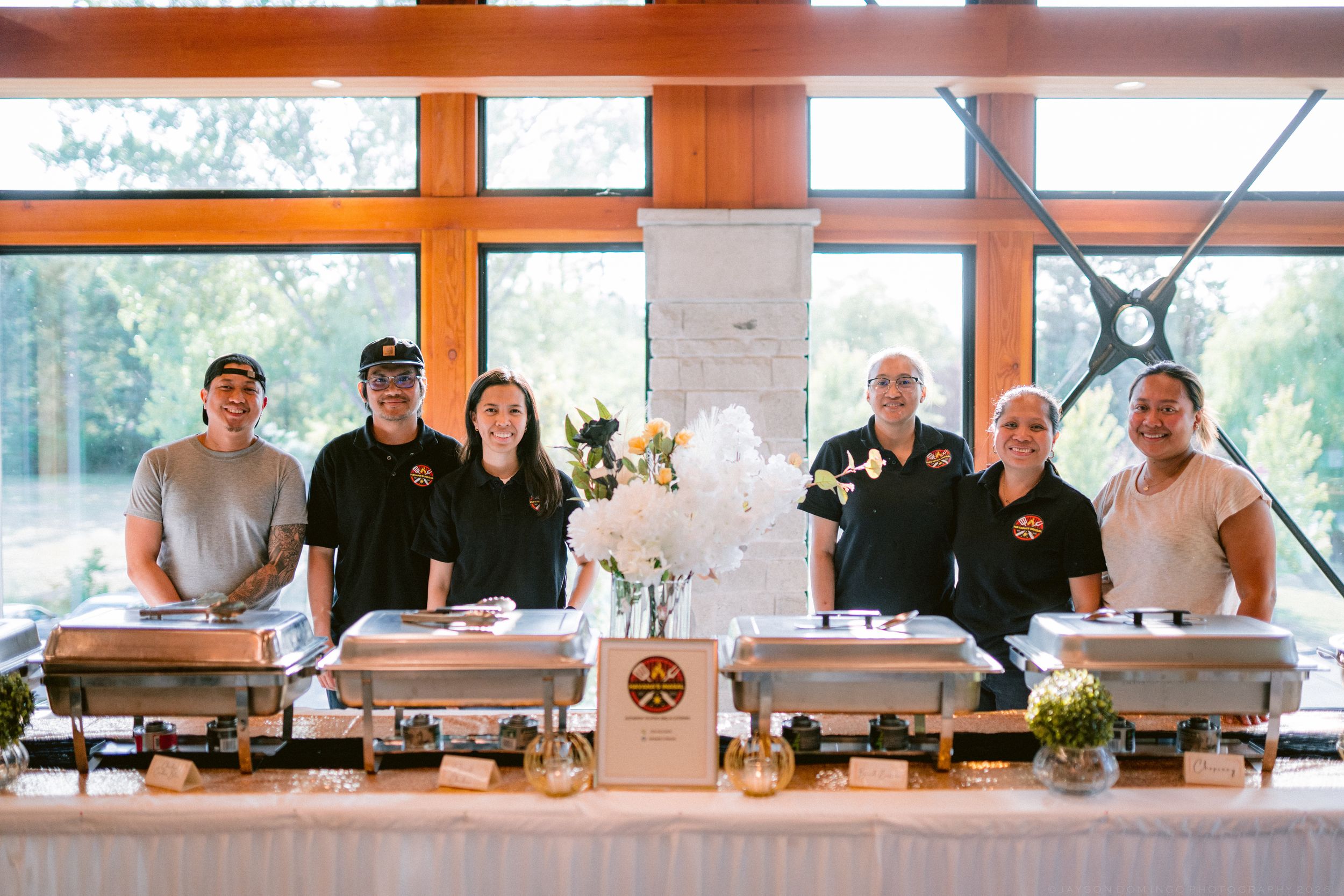 Catering staff smiling behind buffet chafing dishes at a wedding reception venue.