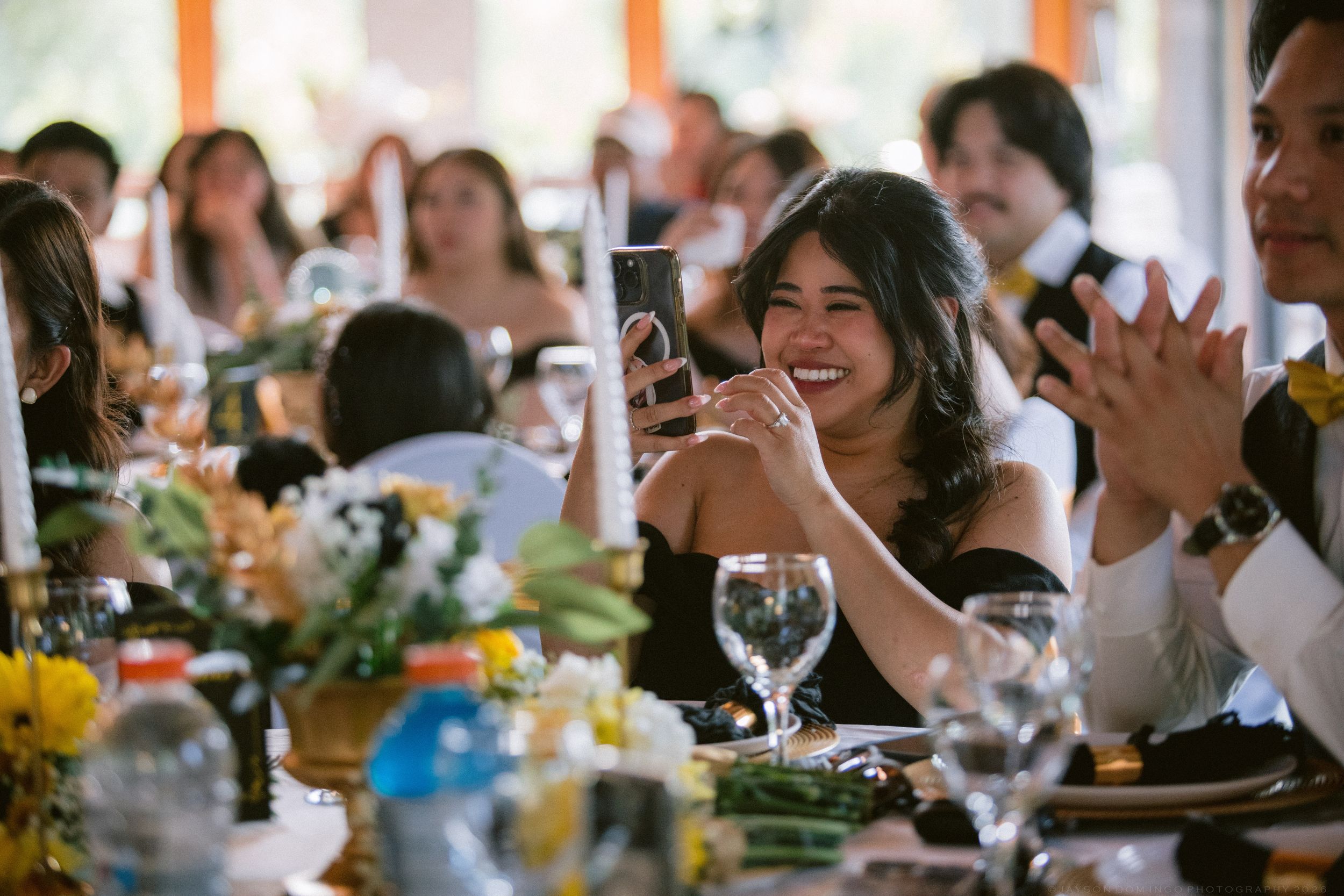 A smiling wedding guest takes a photo on her phone at a beautifully decorated reception dinner table.