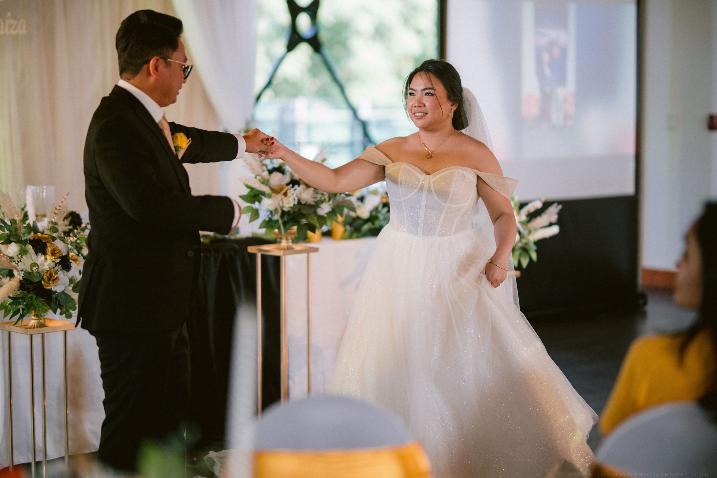 Bride in strapless white ball gown and groom in black suit sharing a joyful first dance moment.
