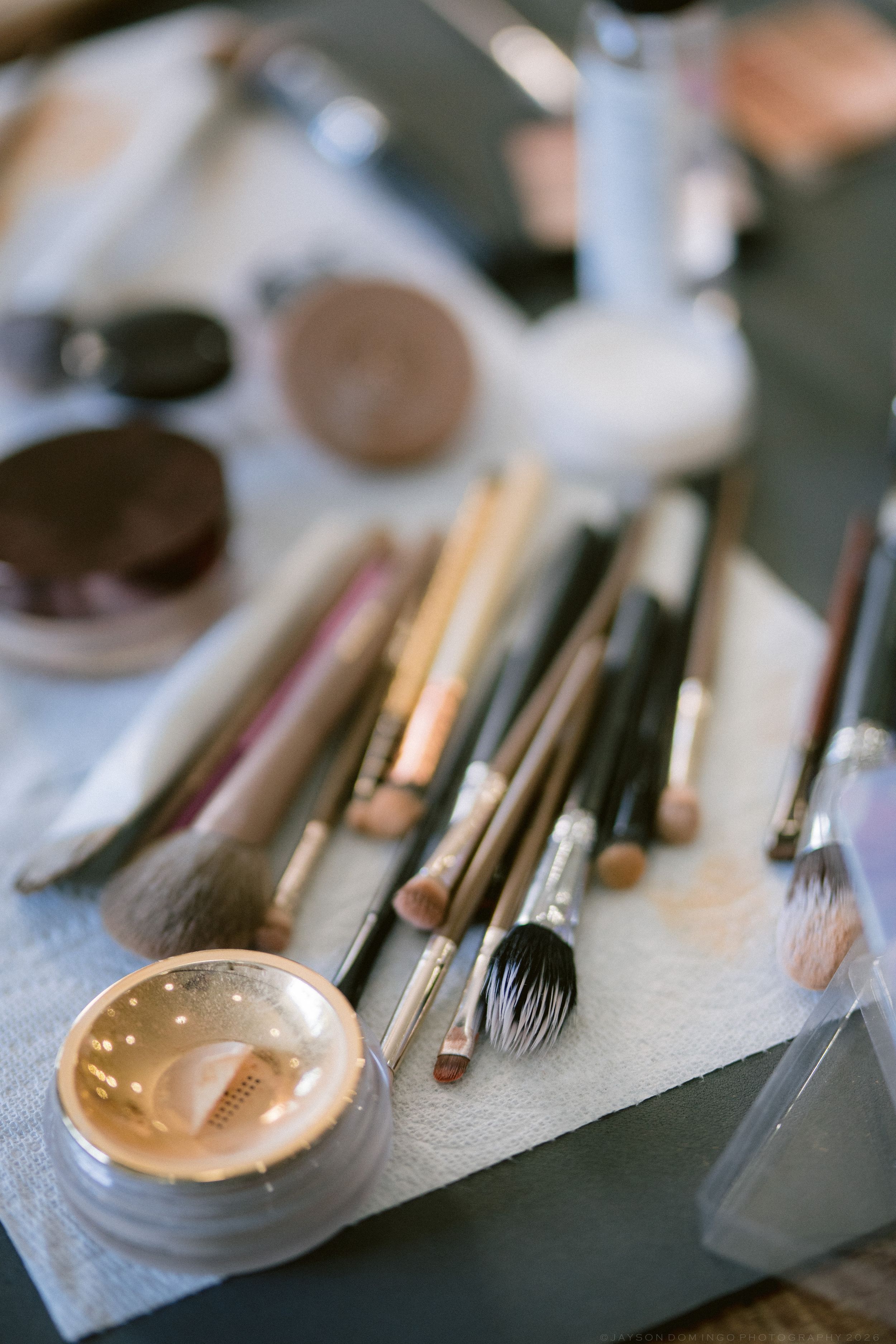 Assorted makeup brushes and cosmetics arranged on a white surface for bridal preparation.