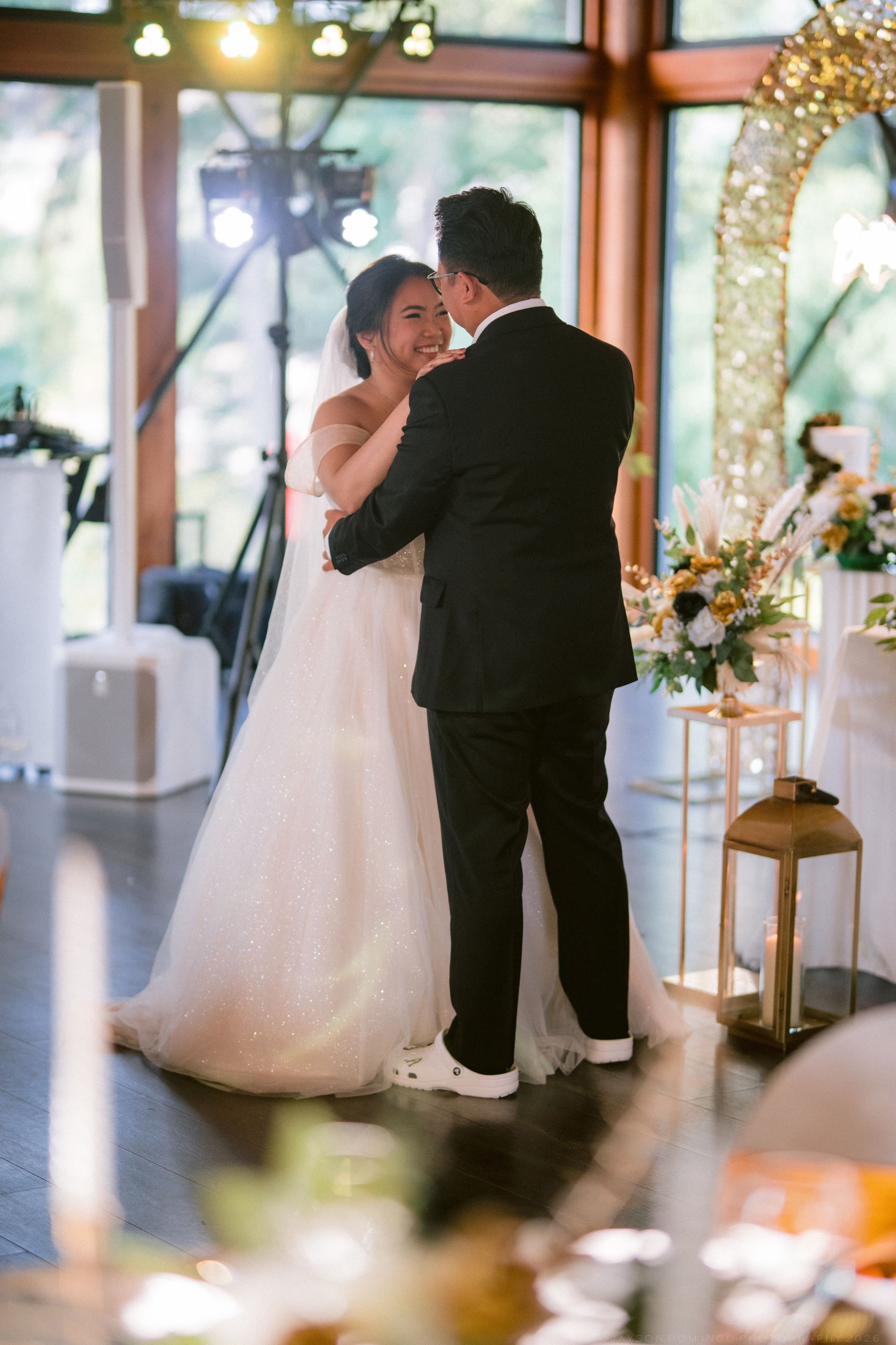 A smiling bride in a white gown shares her first dance with the groom at a wedding reception.