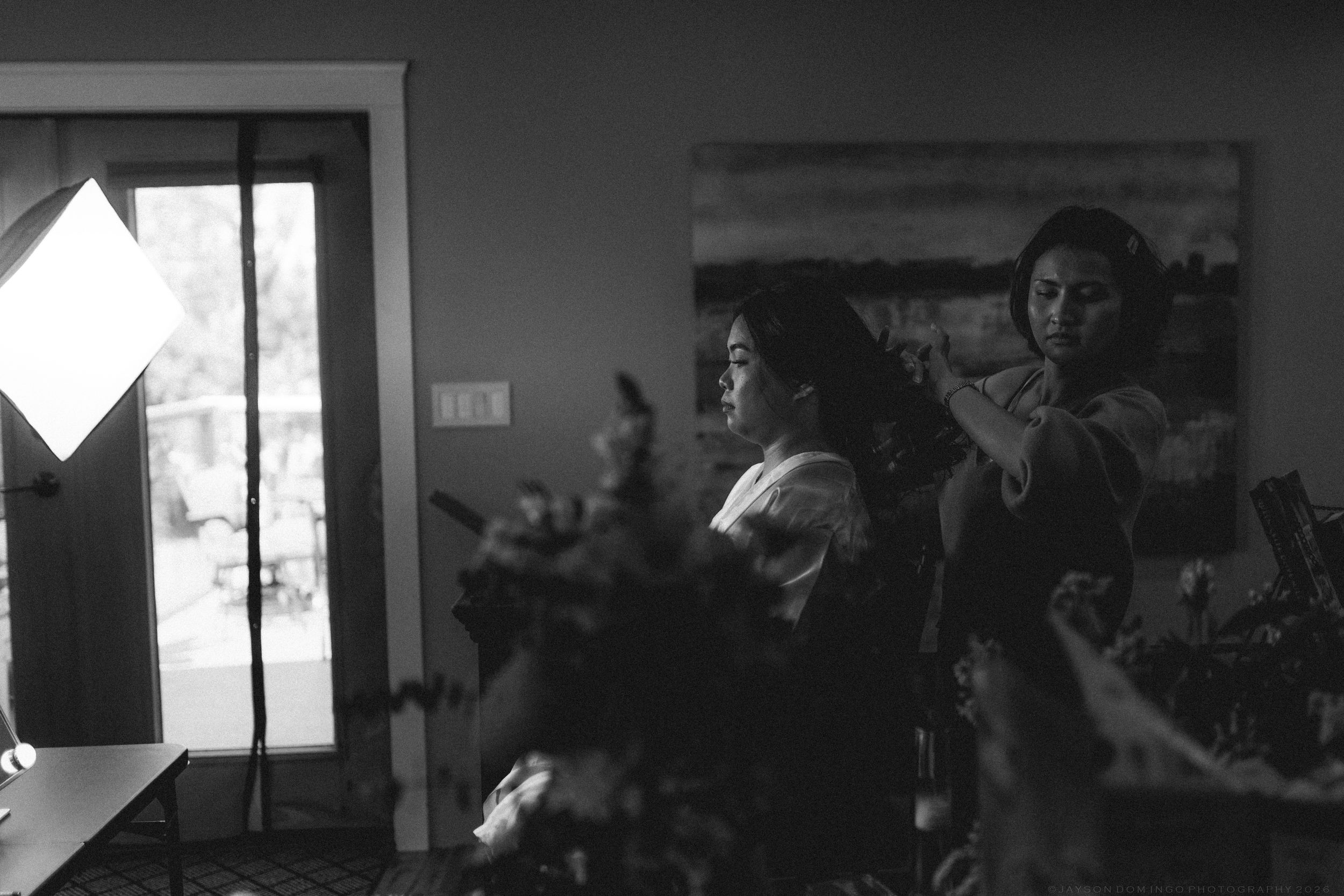 Black and white photo of two women in a softly lit room with floral decor and artwork on the wall.