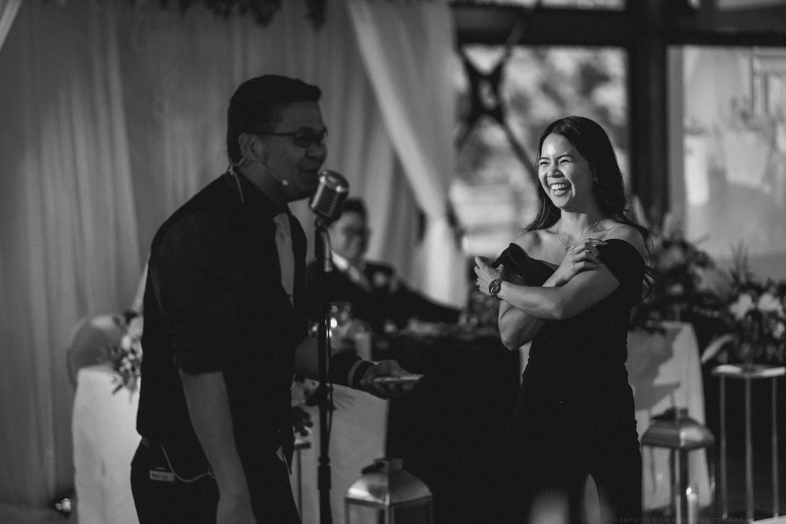 A man and woman share a joyful moment on stage at a wedding reception in black and white.